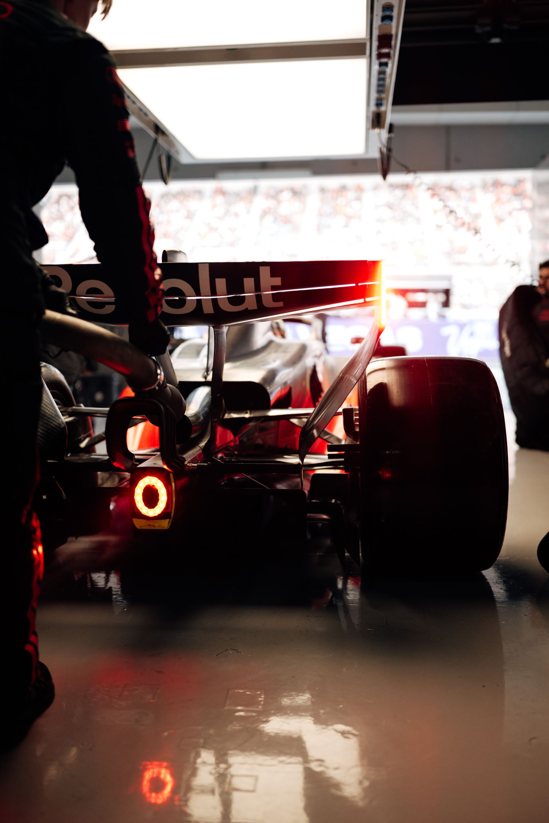 Rear view of the Audi Revolut F1® Team car at the garage exit, glowing light reflected on the floor as crew members stand nearby.