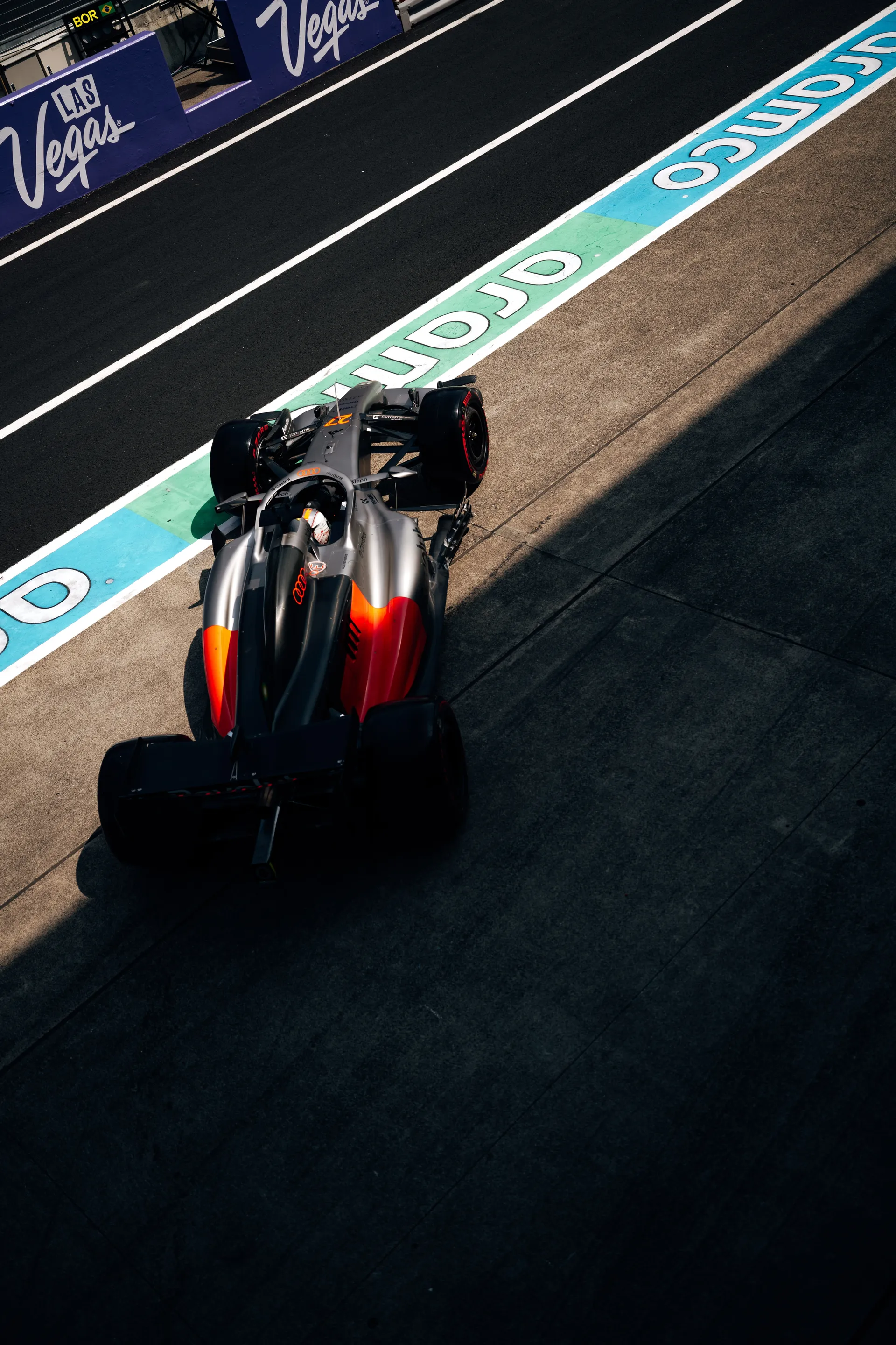 High angle shot of an Audi Revolut F1® Team car running along the Suzuka pit lane near the turquoise lane markings.