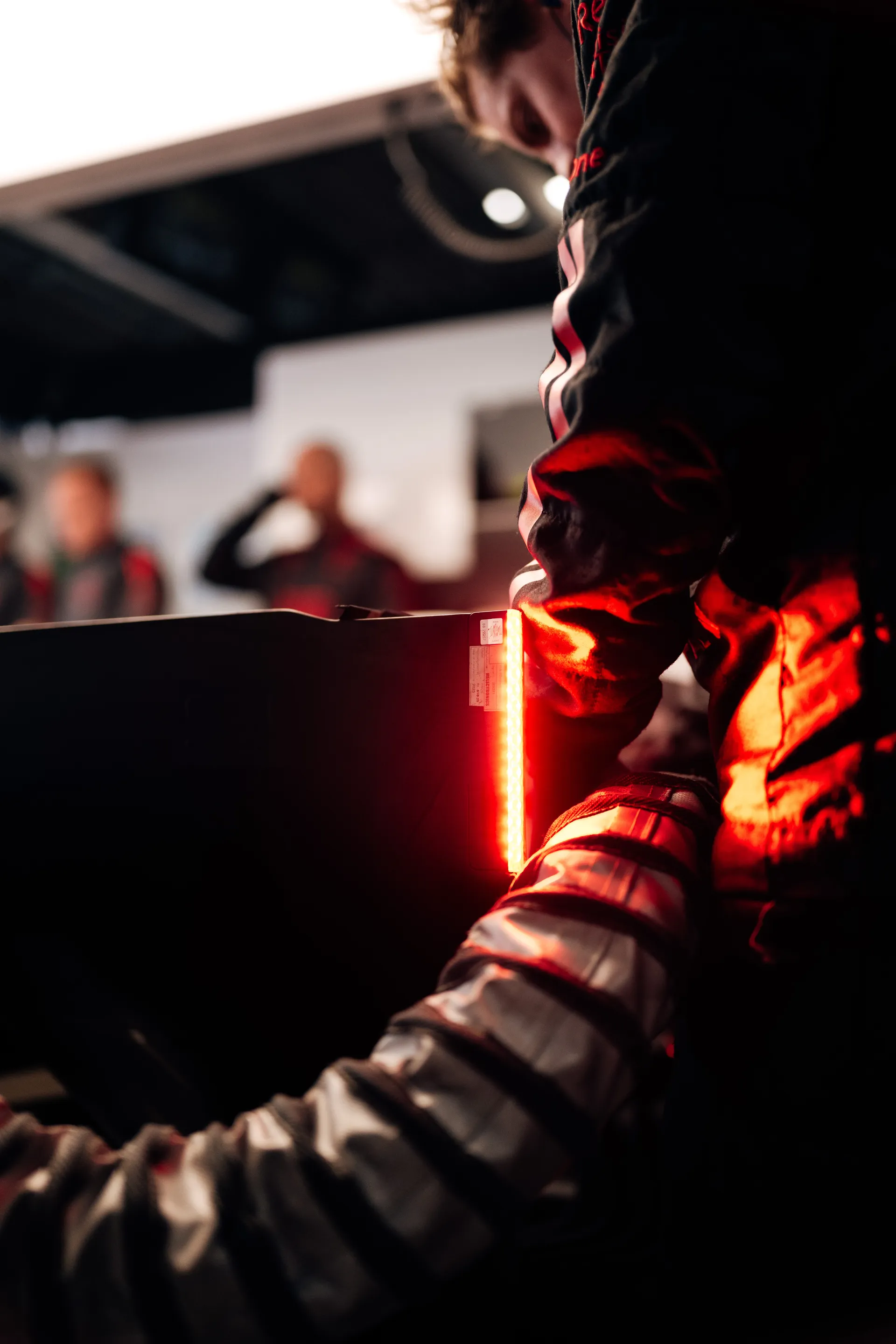 Close detail of a crew member leaning over equipment in the garage, lit by a bright red light strip.