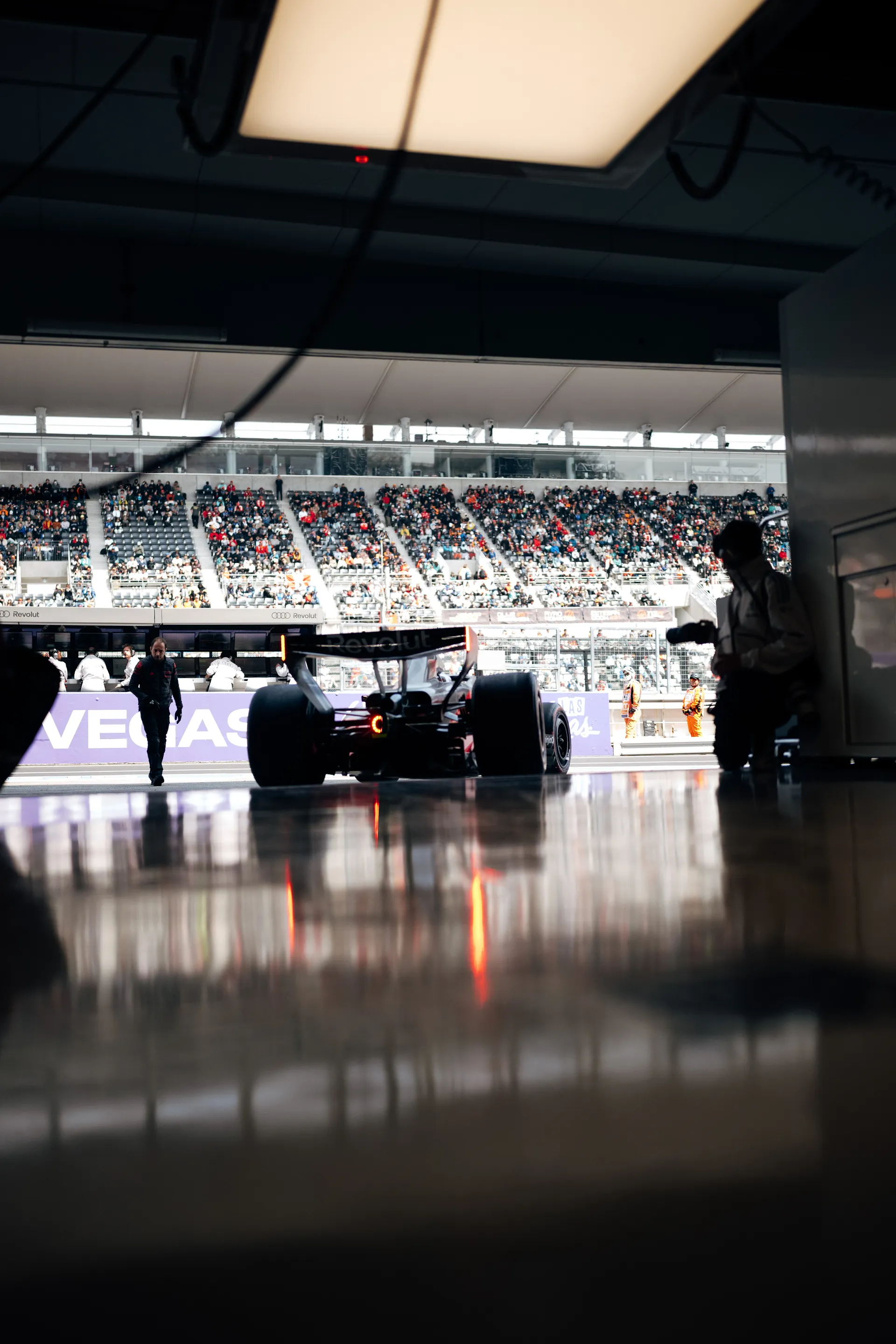 Rear view from inside the garage of an Audi Revolut F1® Team car heading out toward the Suzuka pit lane with grandstands visible outside.