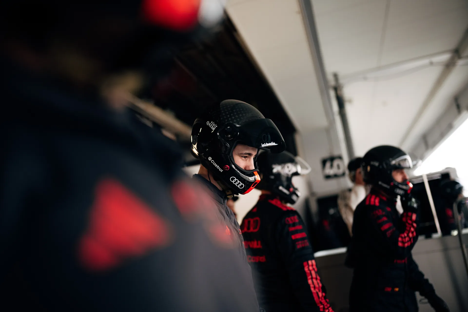 Three Audi Revolut F1® Team crew members in black helmets wait inside the garage during pit lane operations.