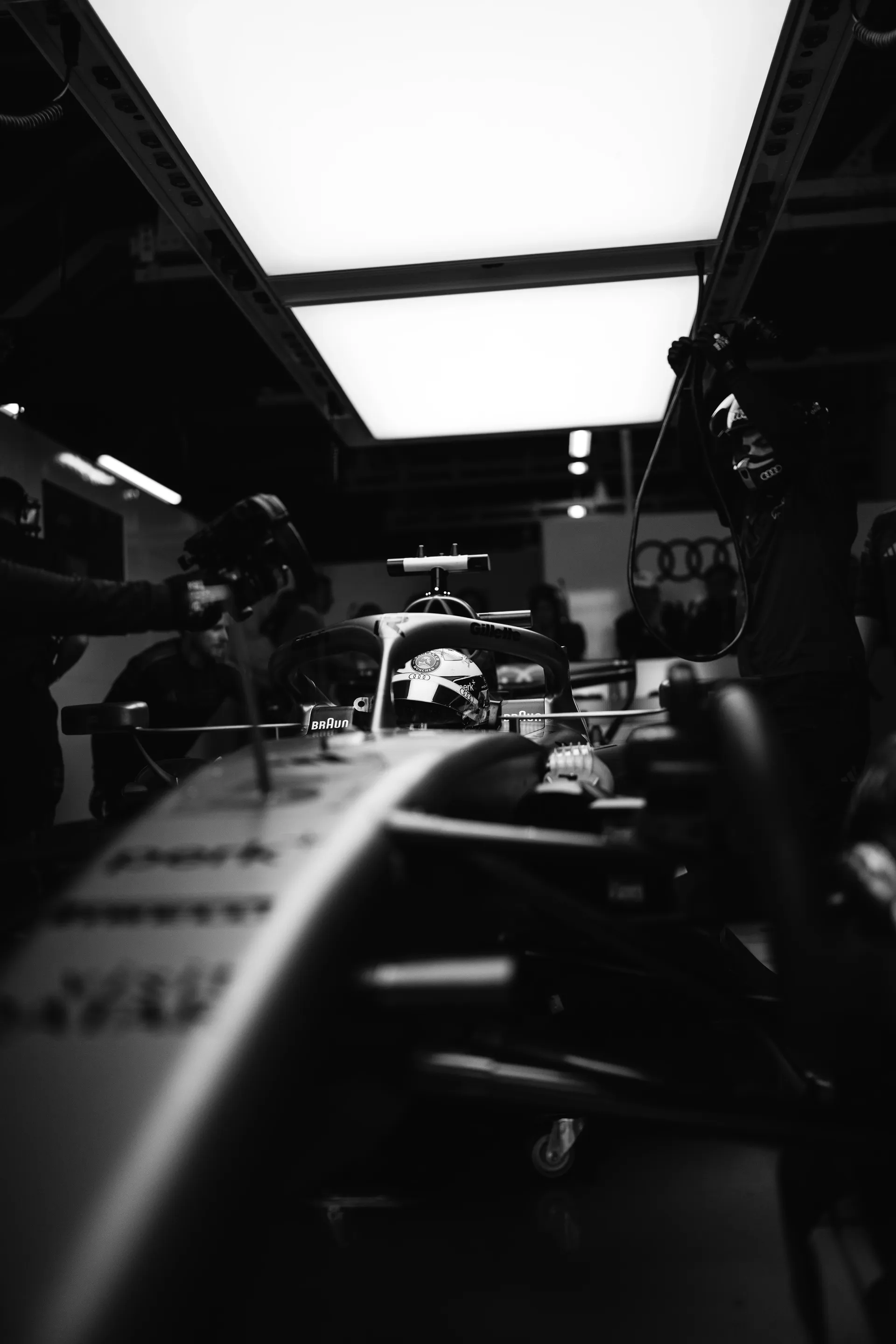 Black and white garage shot of the Audi Revolut F1® Team car framed from the front with mechanics working around it.
