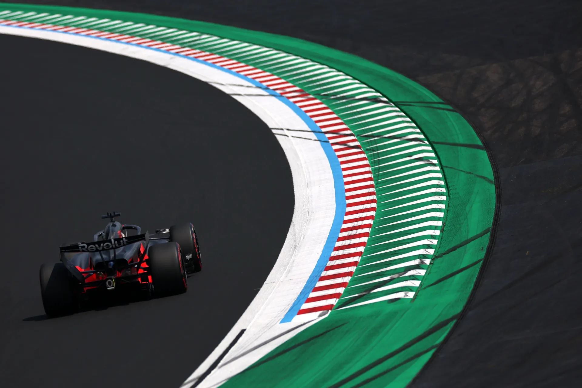 Rear view of the Audi Revolut F1® Team car sweeping through a Suzuka corner beside the green, white, red, and blue curbs.