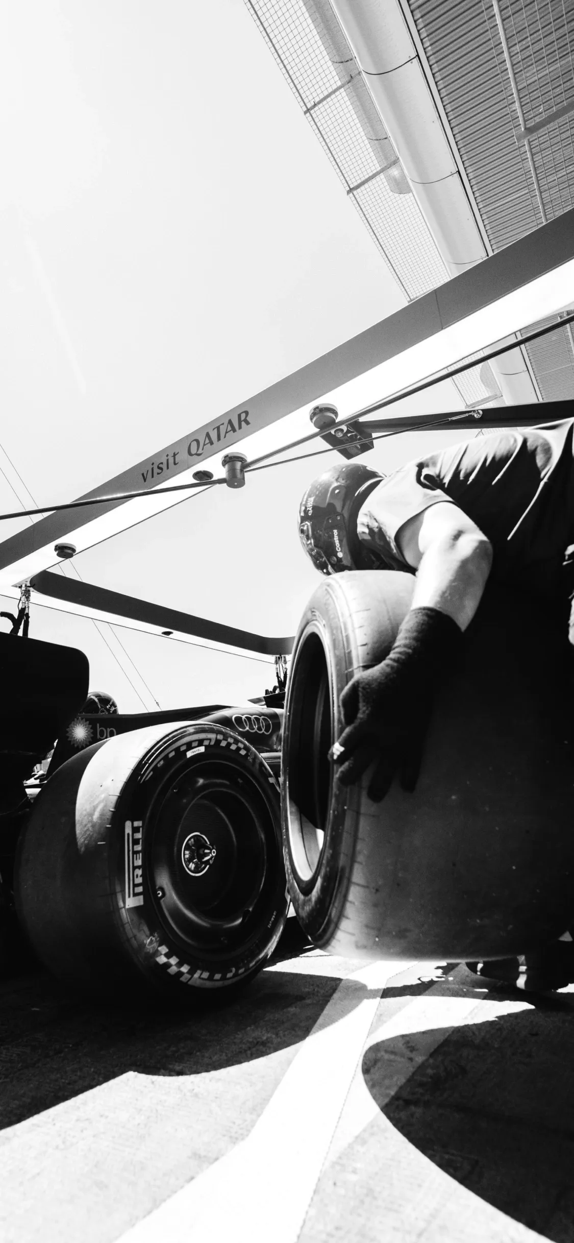 Low-angle black-and-white shot of a Formula 1 car in the garage, focusing on the rear tire and mechanical details of the Audi Revolut F1® Team car