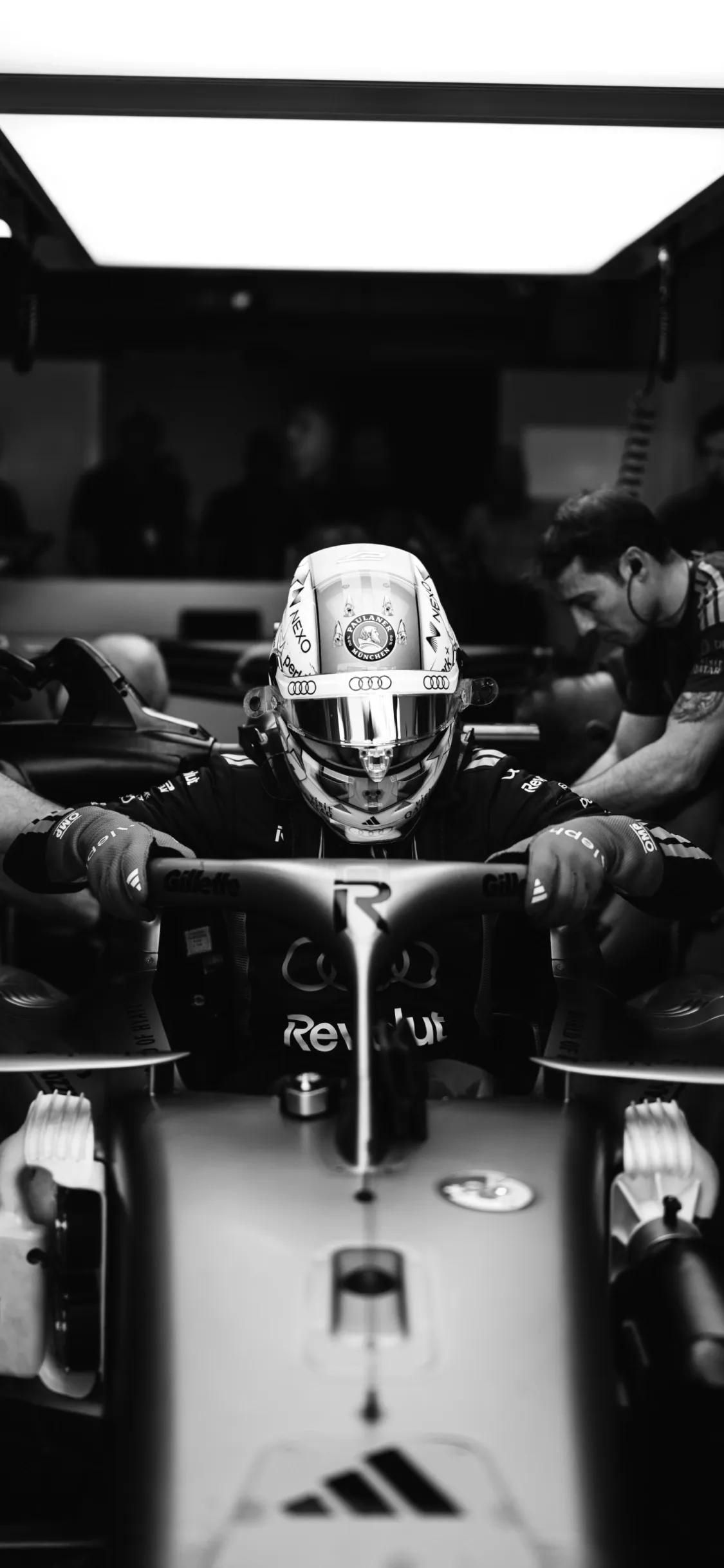 Front-facing dramatic black-and-white image of a driver sitting in the cockpit, hands on the wheel, capturing focus and intensity of the Audi Revolut F1® Team