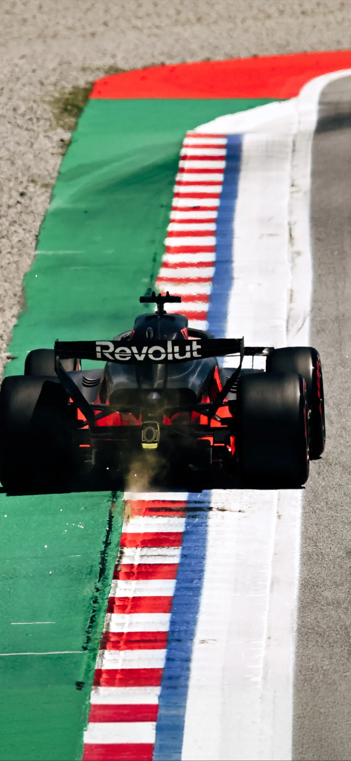 Rear view of a Formula 1 car driving along the track edge with red-white curbs, highlighting race dynamics of the Audi Revolut F1® Team