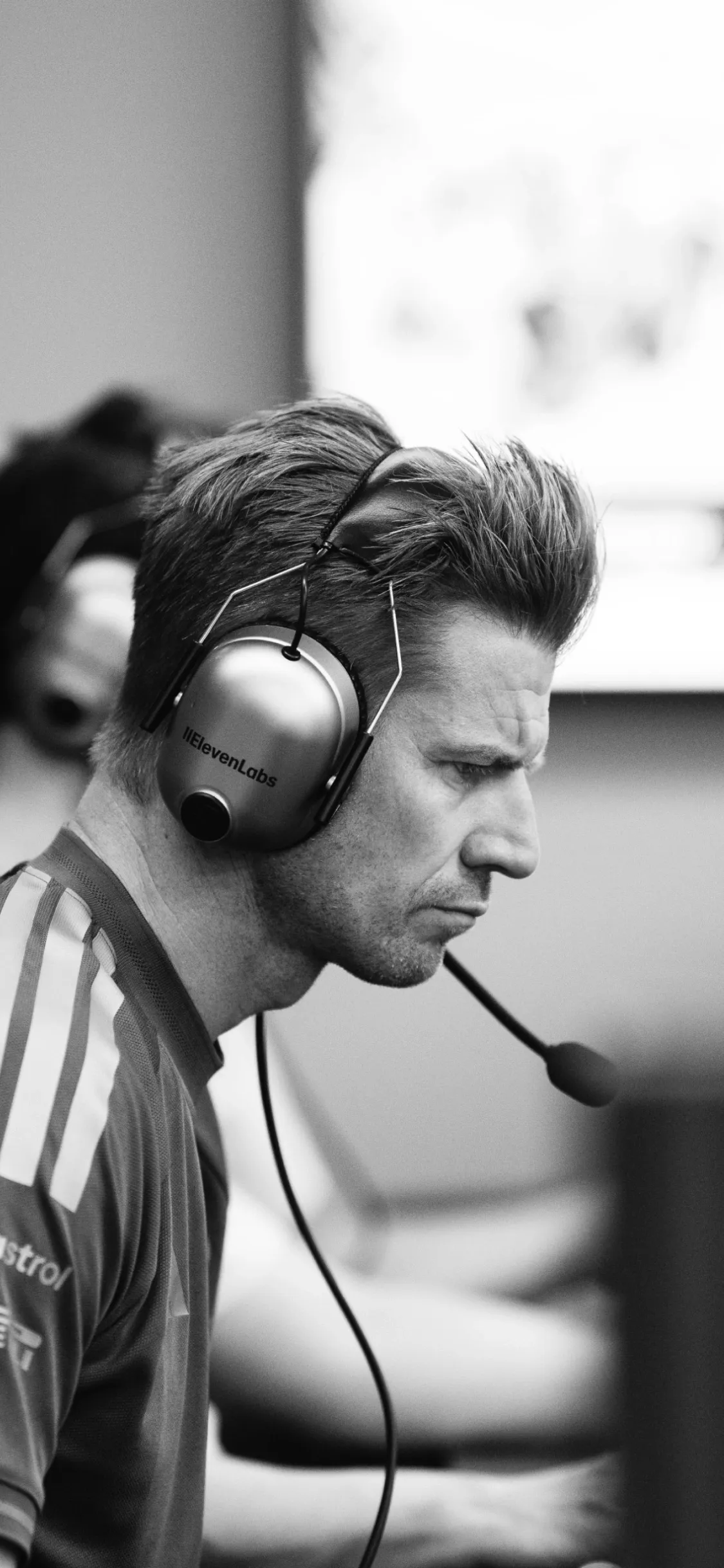 Black-and-white close-up of Nico Hulkenberg wearing a headset, concentrating during live operations for the Audi Revolut F1® Team