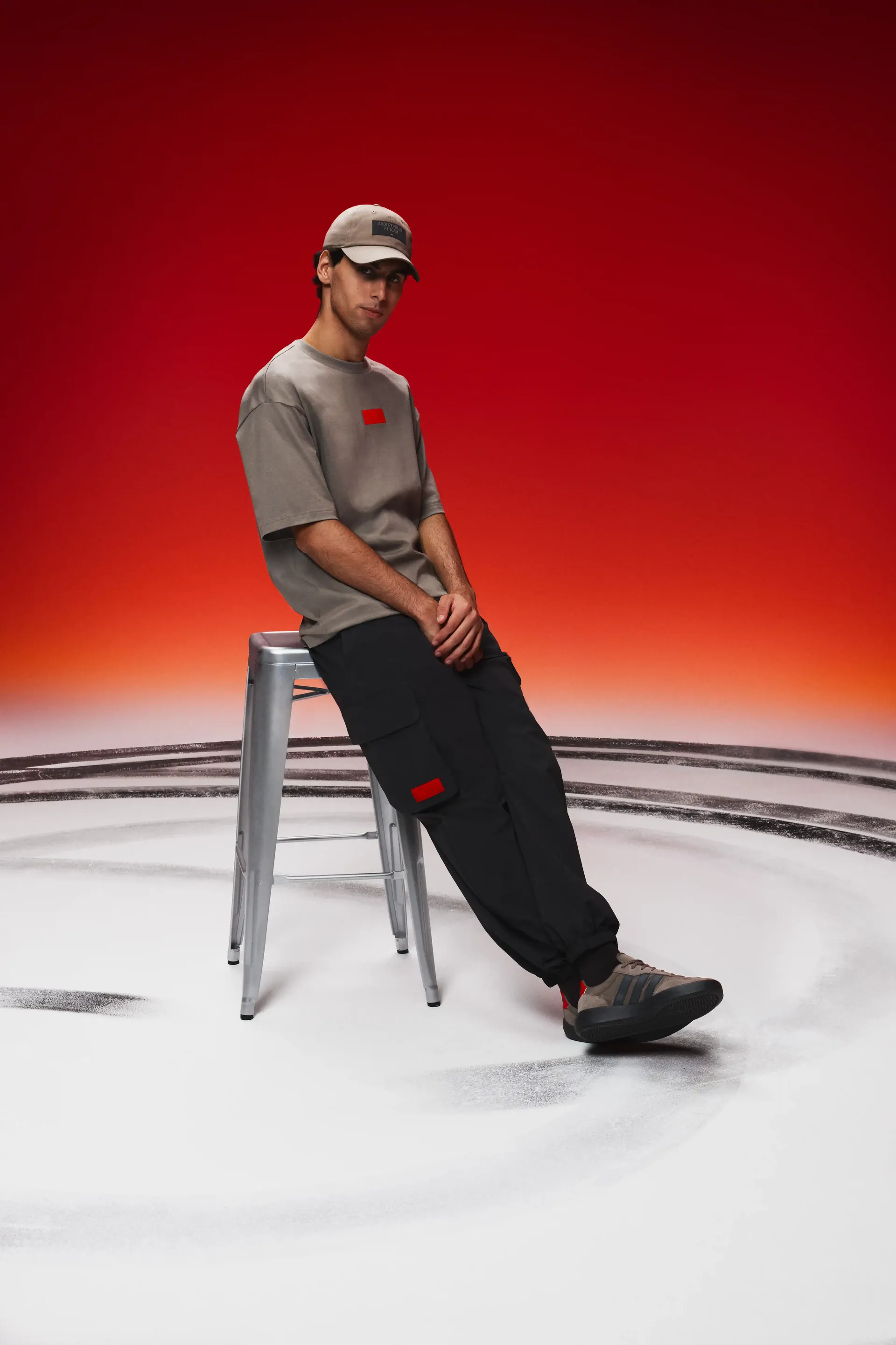 Formula 1 driver Gabriel Bortoleto in brown team shirt and cap casual seated pose on stool dynamic studio lighting clear focus on fanwear and athlete posture
