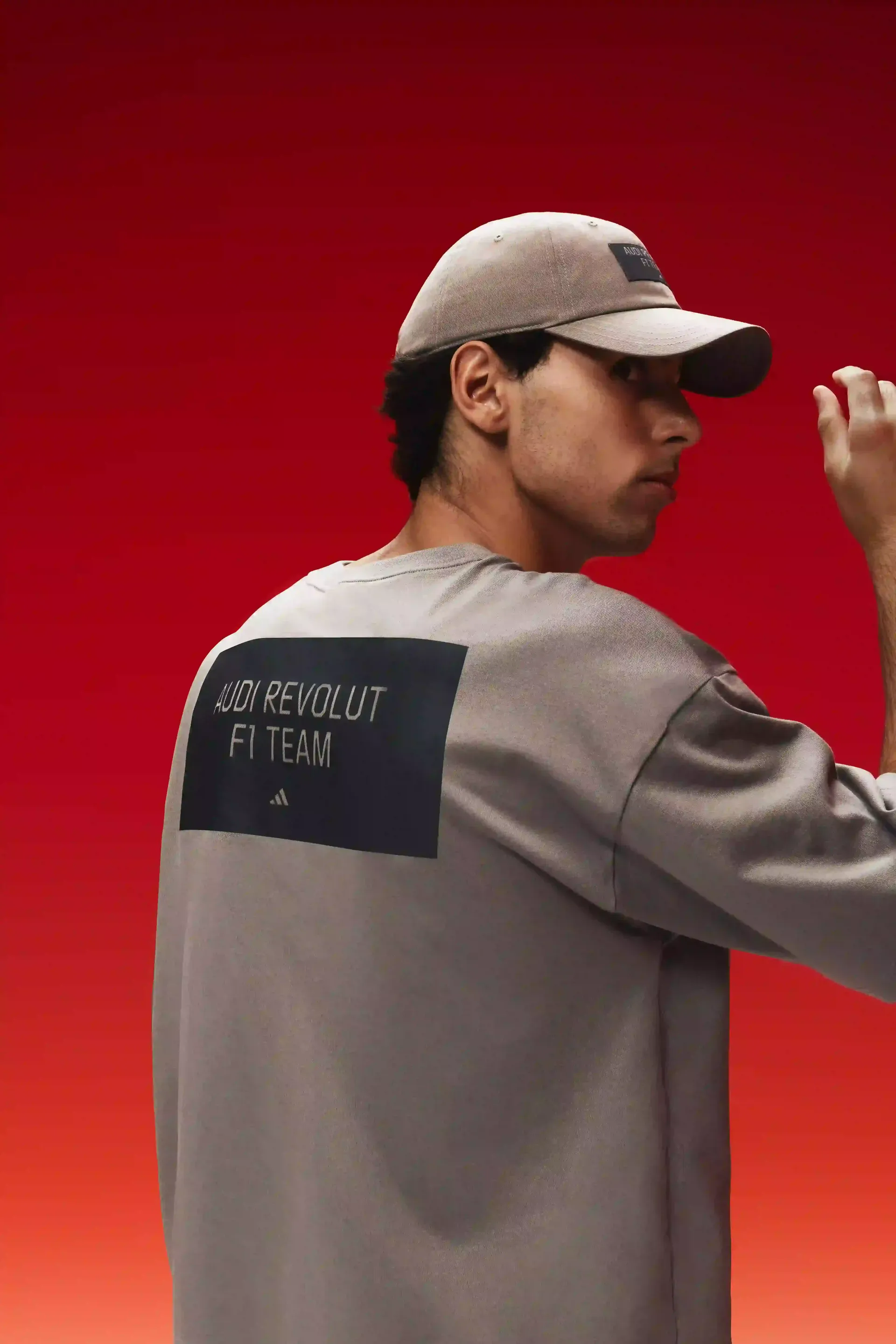 Formula 1 driver Gabriel Bortoleto seen from behind wearing a light-brown team shirt, visible back branding, cap, red studio background, focus on team identity.