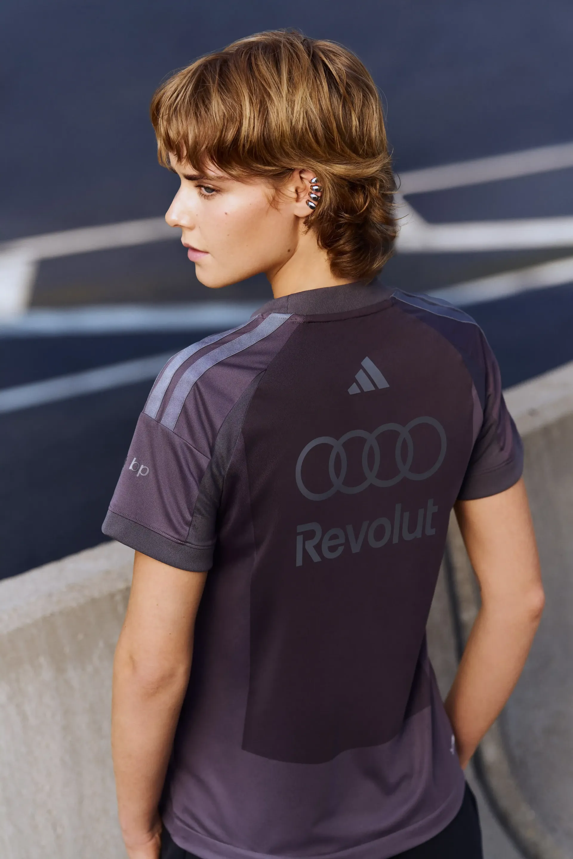 Young model in grey team short sleeve shirt back view visible branding urban background modern motorsport aesthetic