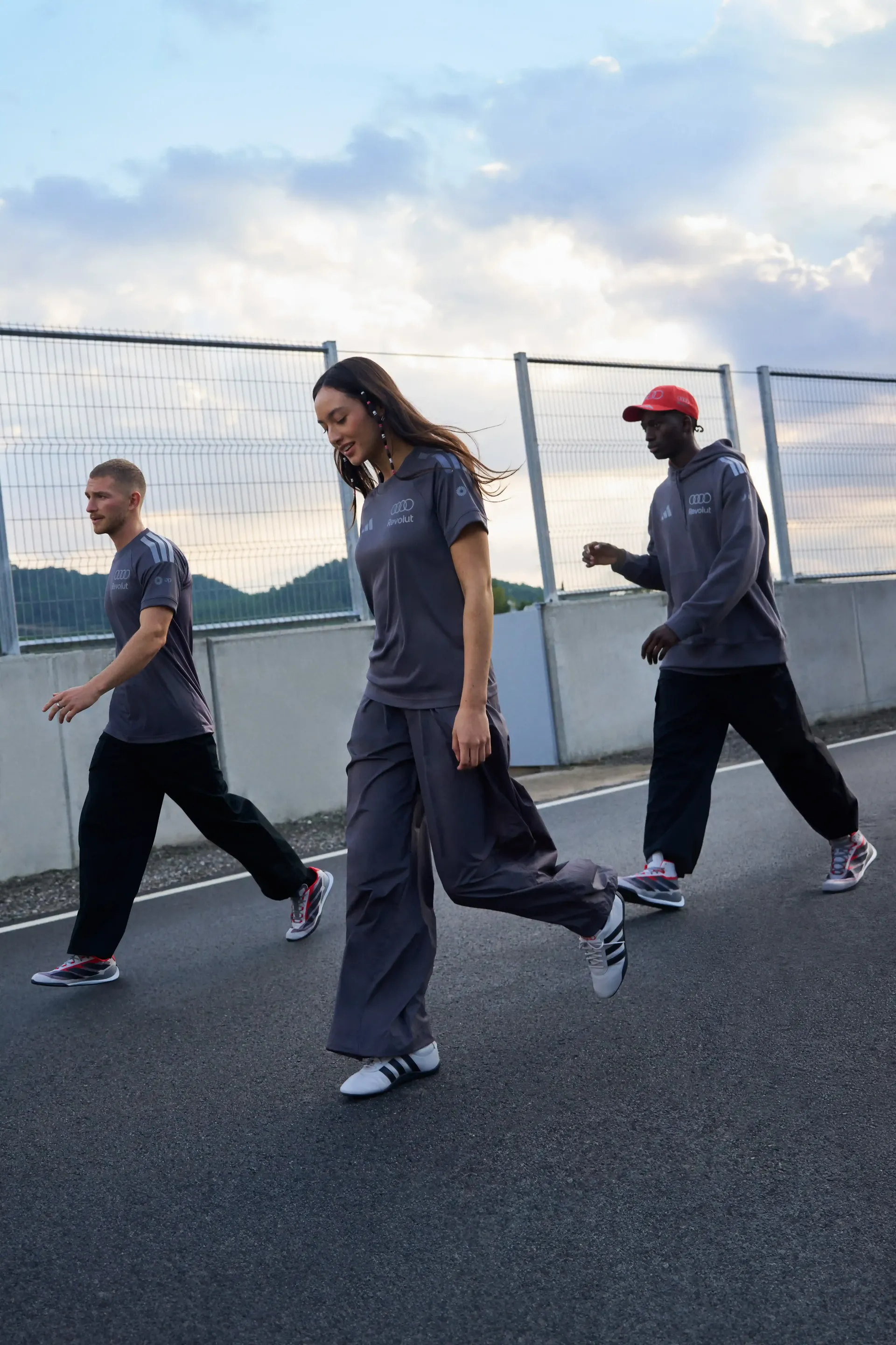Multiple models walking side by side on paved surface relaxed stride teamwear styling authentic streetwear atmosphere