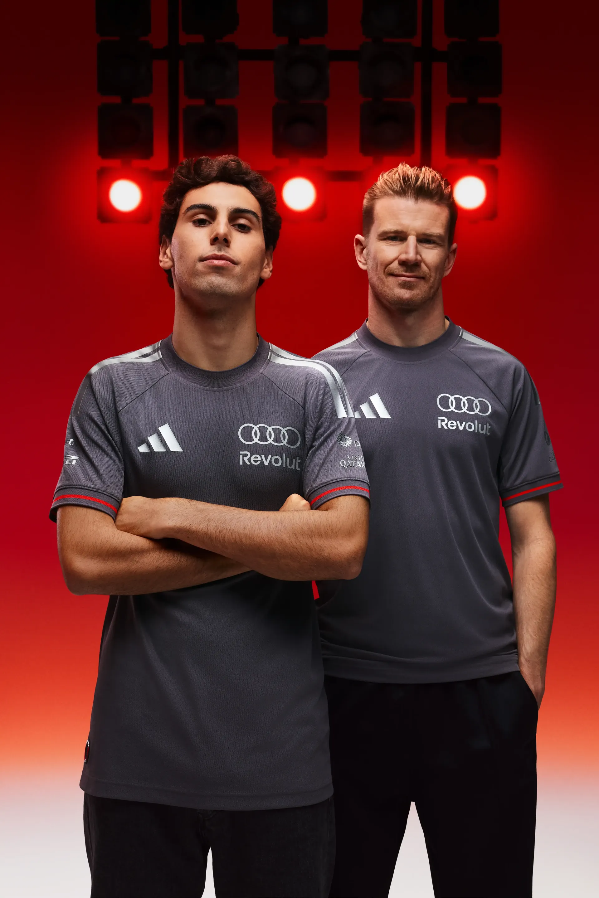 Two Formula 1 drivers Gabriel Bortoleto and Nico Hulkenberg standing half-portrait grey team shirts confident posture arms crossed second Nico Hulkenberg slightly offset professional motorsport team look red studio background