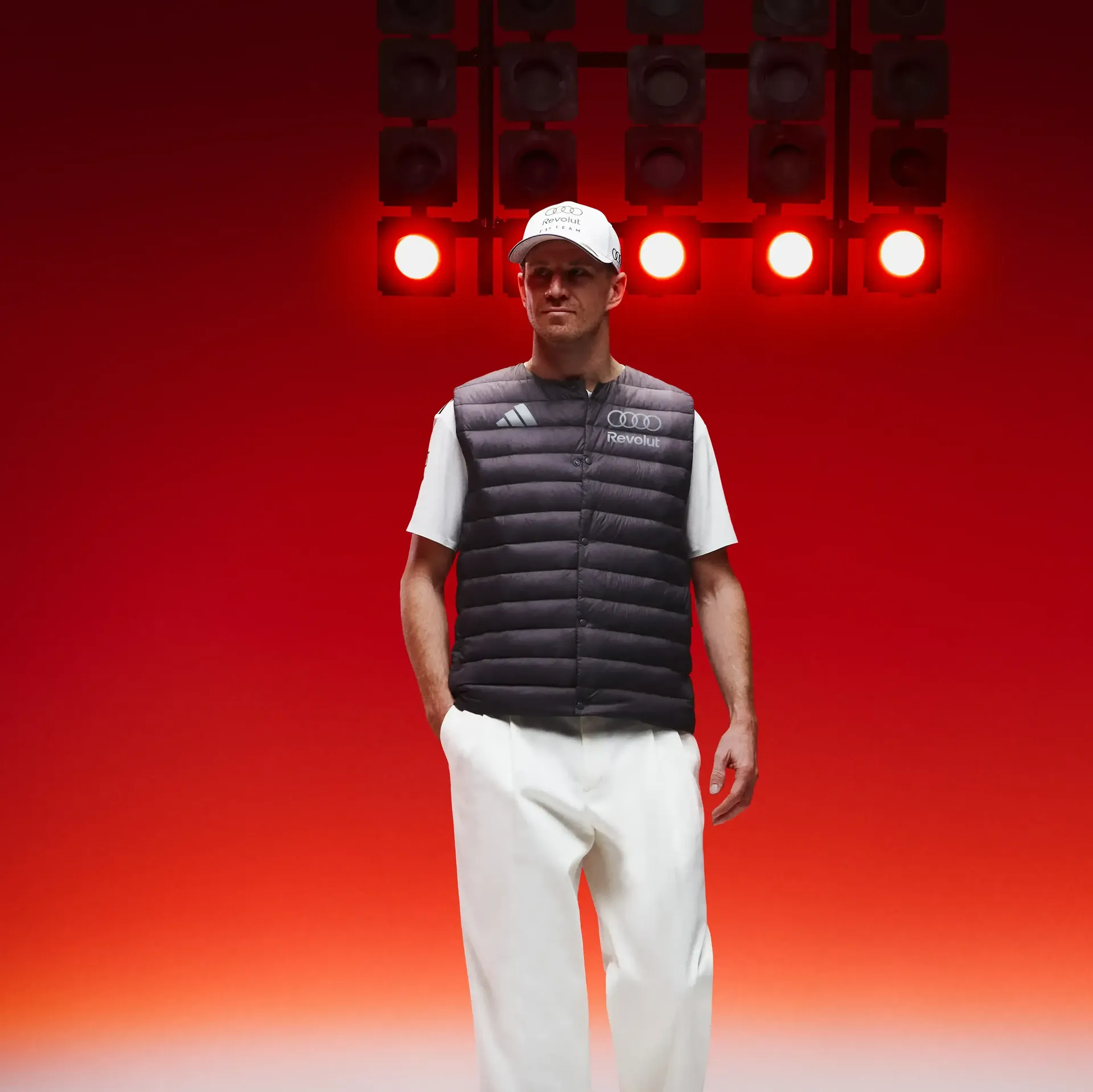 Full body shot of Formula 1 driver Nico Hulkenberg light pants team vest clearly defined studio floor red motorsport background modern performance look