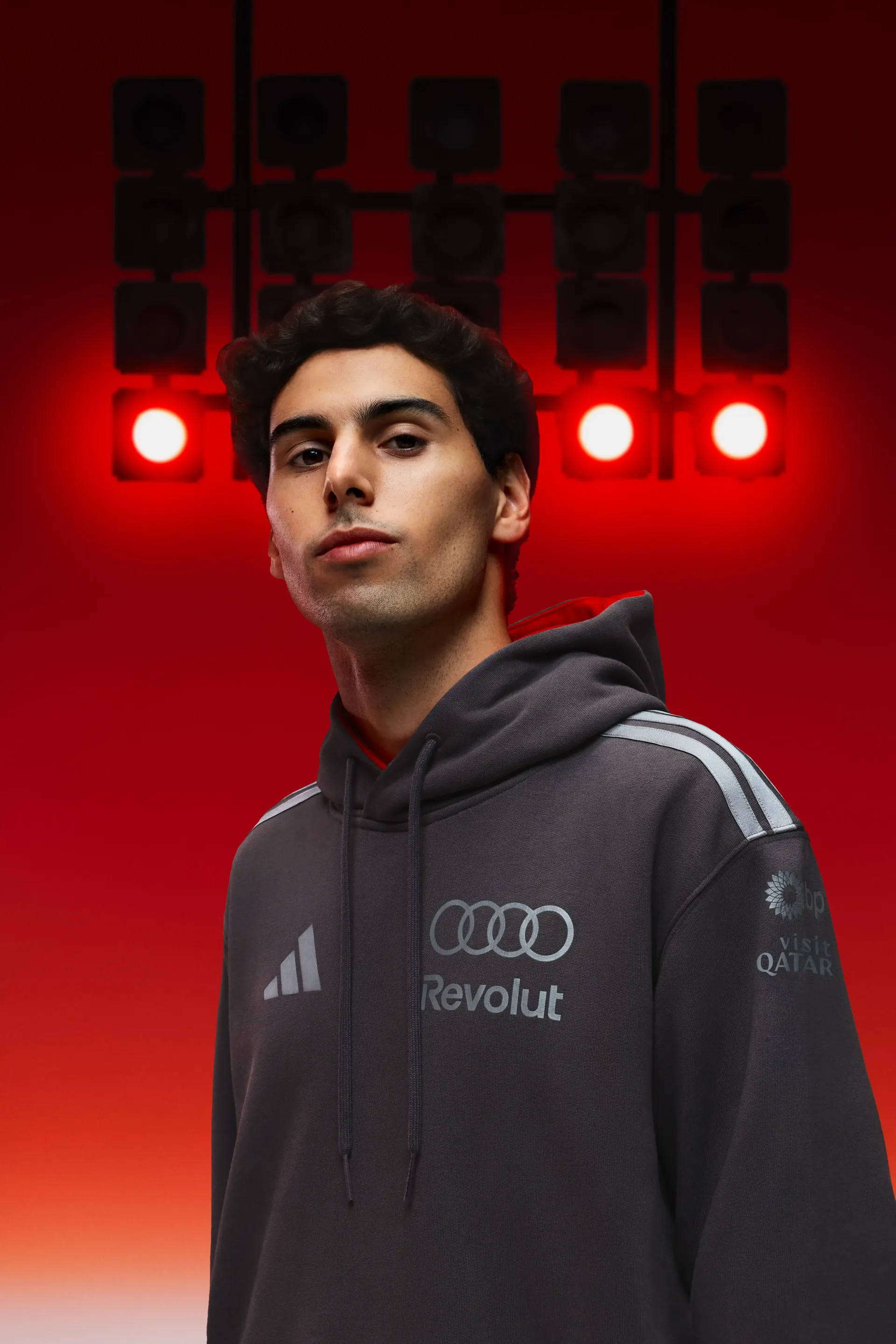 Formula 1 athlete Gabriel Bortoleto Revolut Audi team dark hoodie direct camera gaze minimalist studio setup red light gradient focused racing driver presence