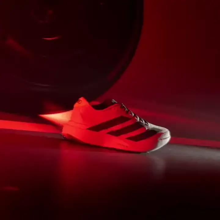 Close up of a white Adidas sneaker three dark stripes red background tire motorsport