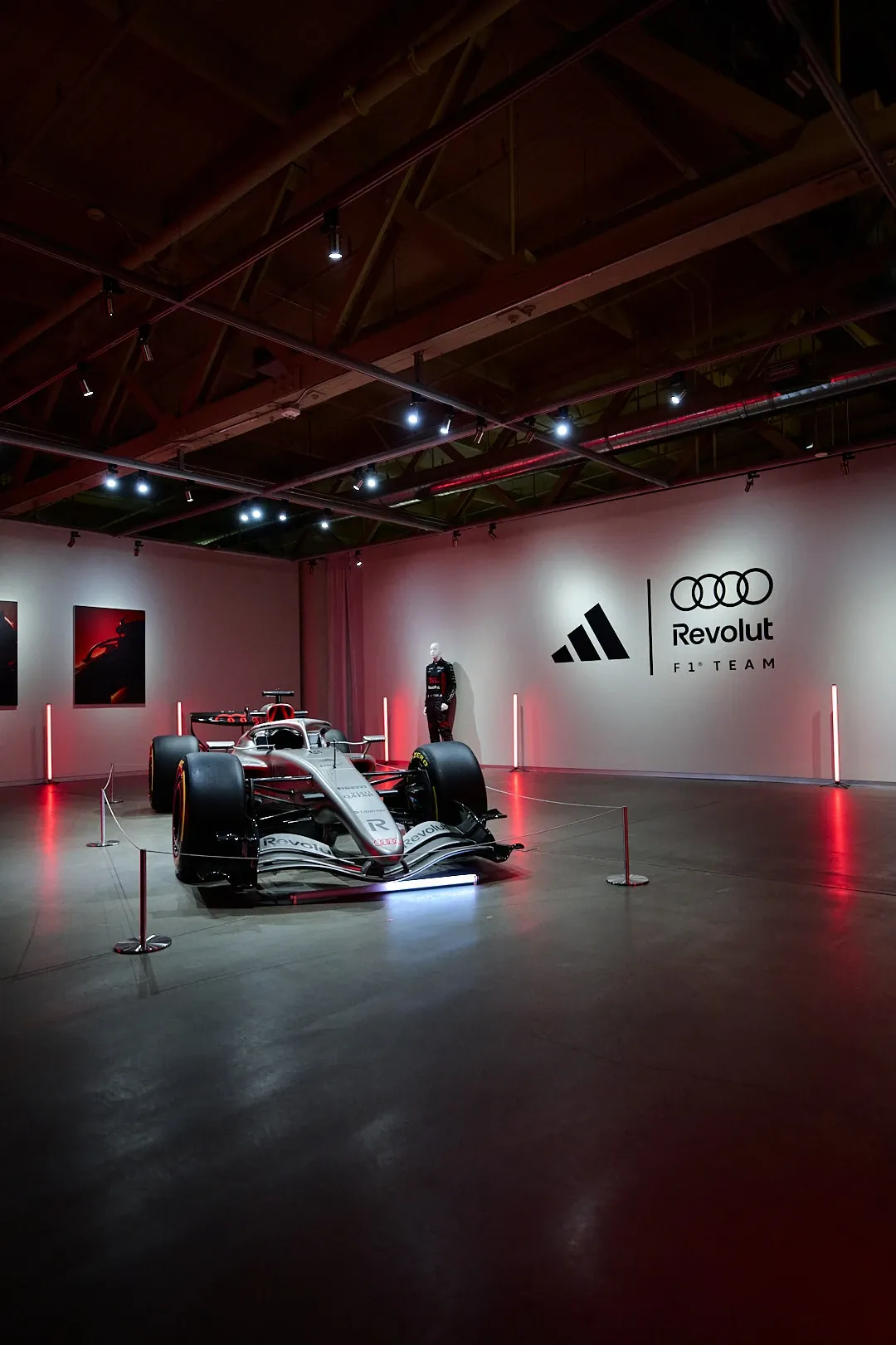 Wide shot of the show car facing the Adidas and team logo wall in a red-lit room.