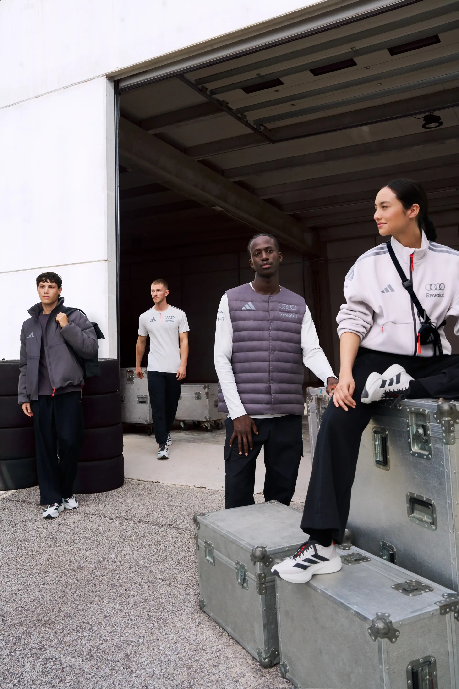 Group of models on concrete blocks in front of industrial building team outfits mix of standing and sitting authentic campaign shot