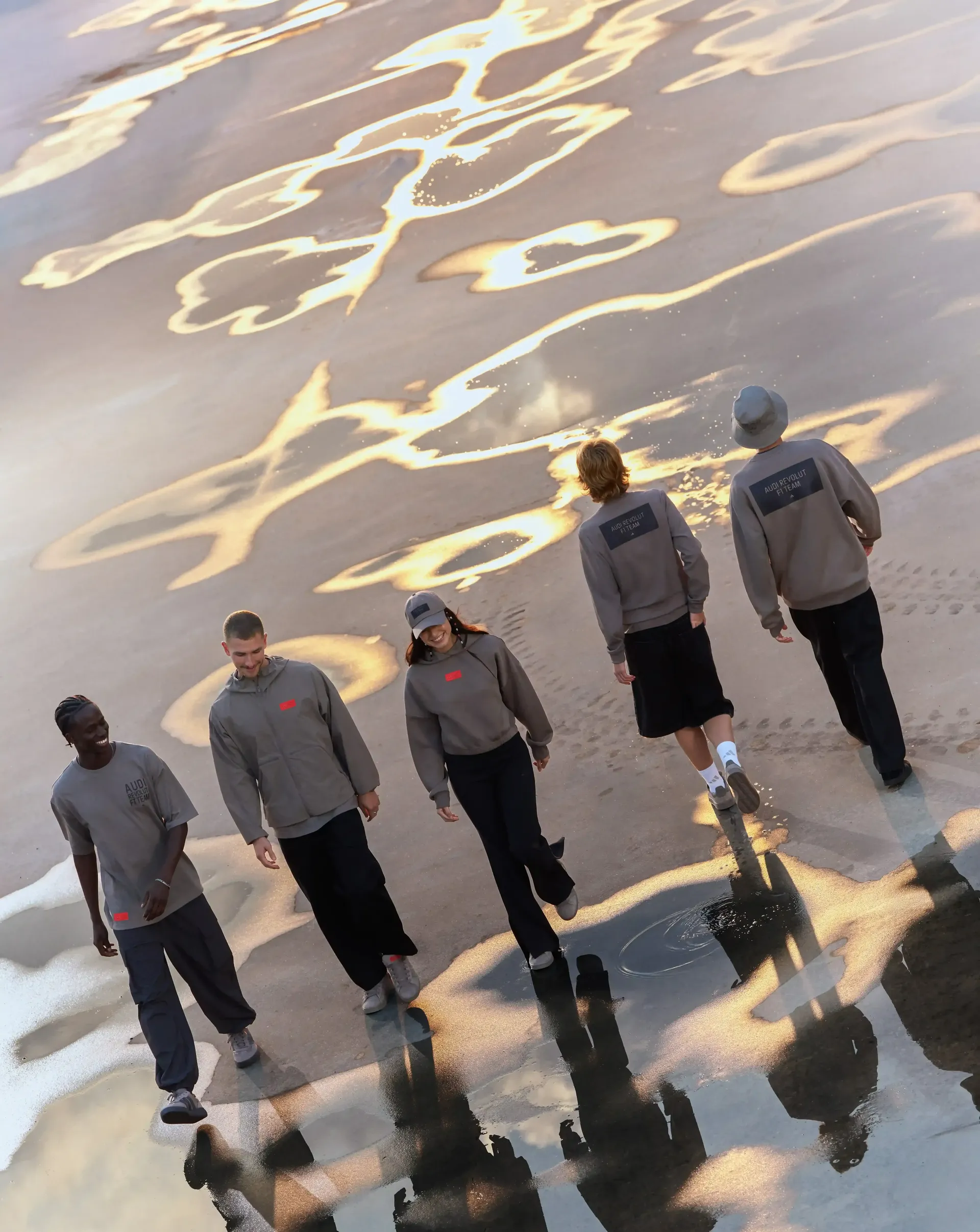 Several models seen from behind wearing gray shirts on an open asphalt surface, with a focus on back view and movement