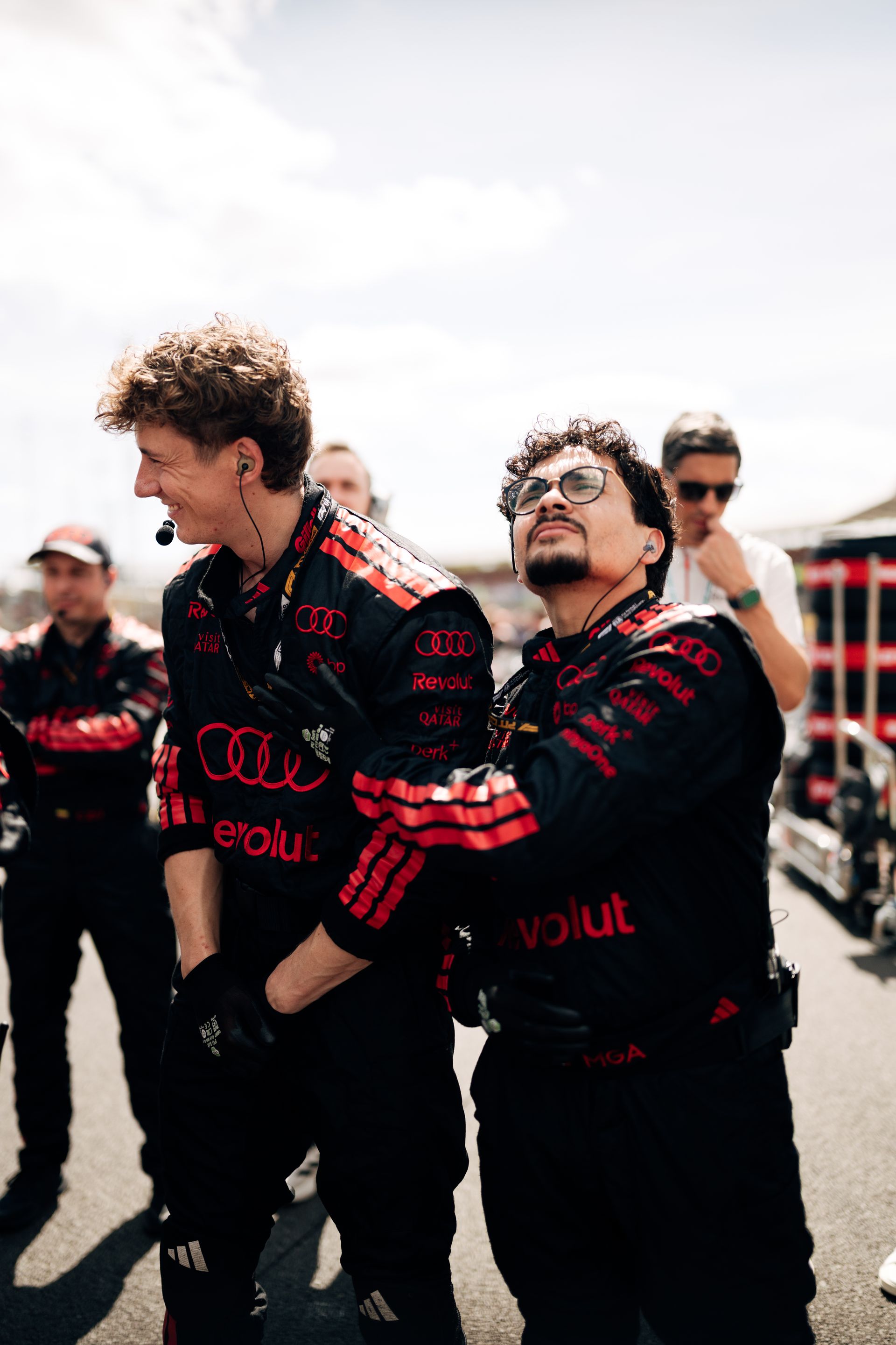 Audi Revolut F1® Team crew members stand on the Silverstone grid ahead of the race, preparing and observing final pre-race moments.