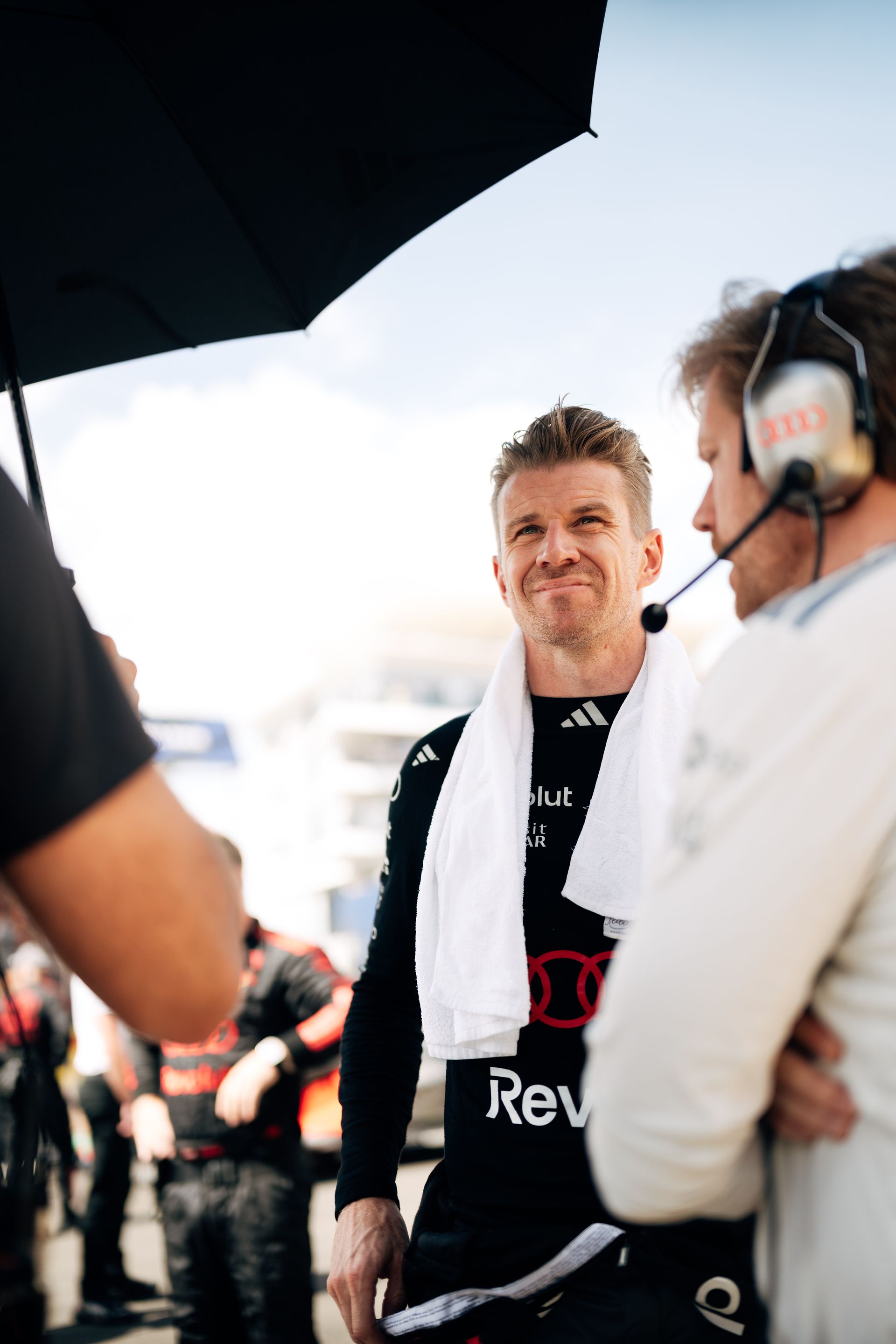 Nico Hulkenberg stands on the grid under an umbrella with Audi Revolut F1® Team engineers, focused ahead of the race start.