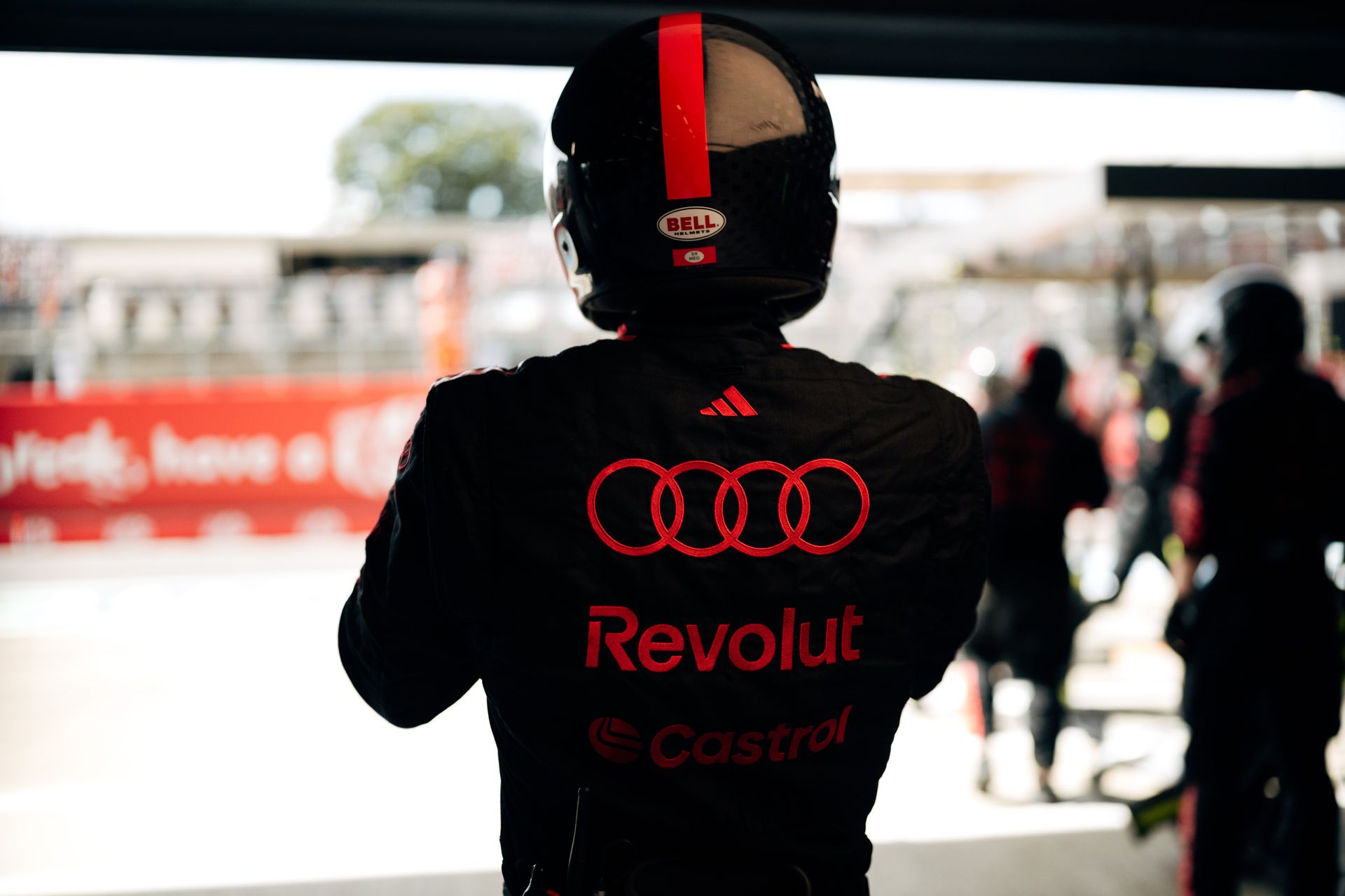 An Audi Revolut F1® Team pit crew member stands at the garage exit, seen from behind with Audi branding, preparing for race action.
