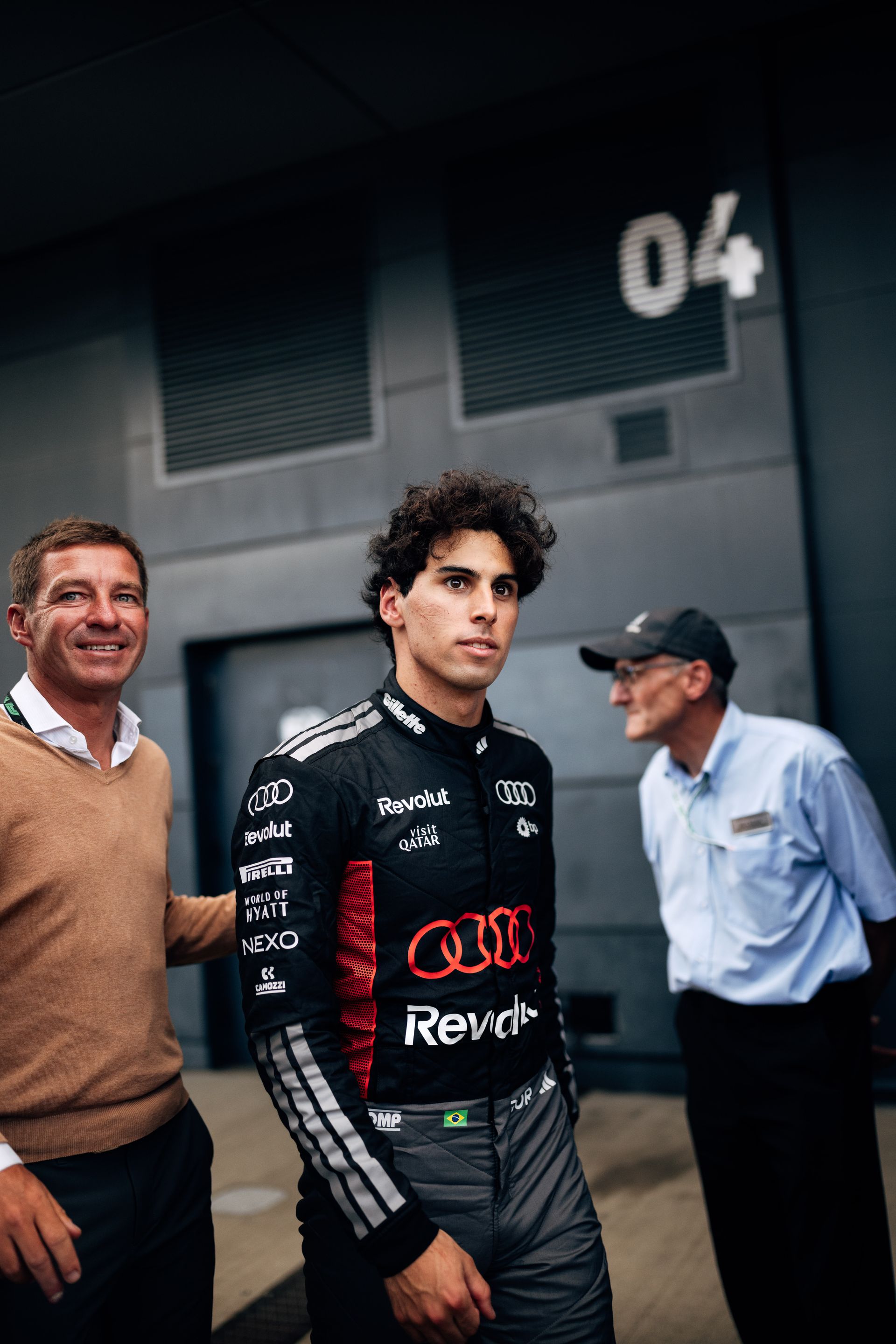 Gabriel Bortoleto stands trackside at Silverstone with team members, focused as the race weekend continues.