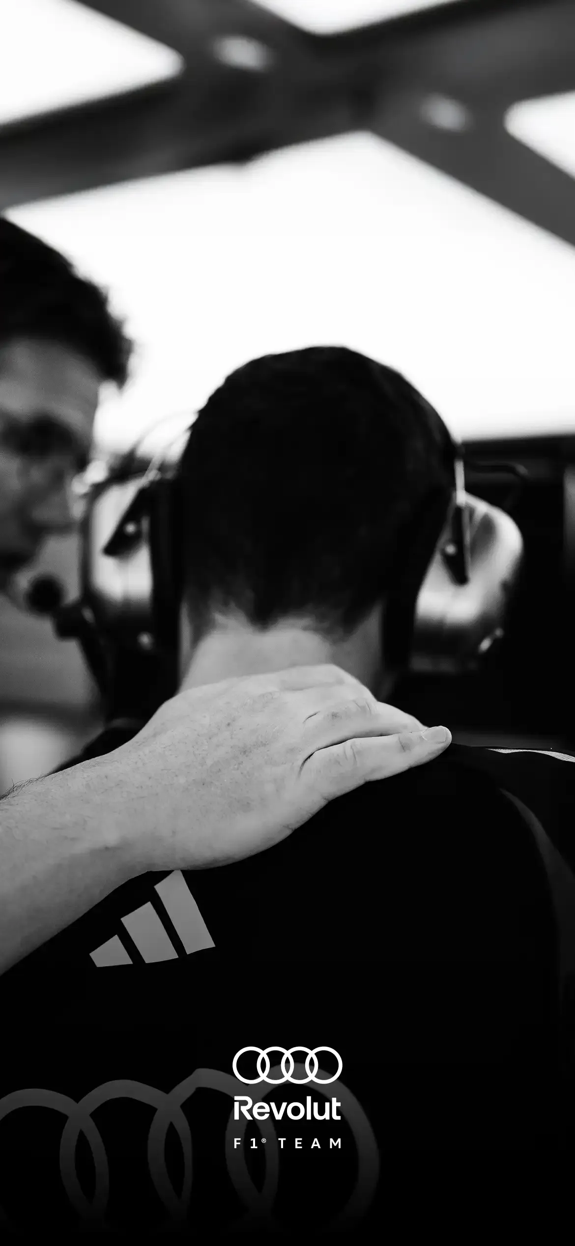 Black and white close up of acrewwmember inside the garage from the back, a hand from a collegue on his shoulder, wearing headphones