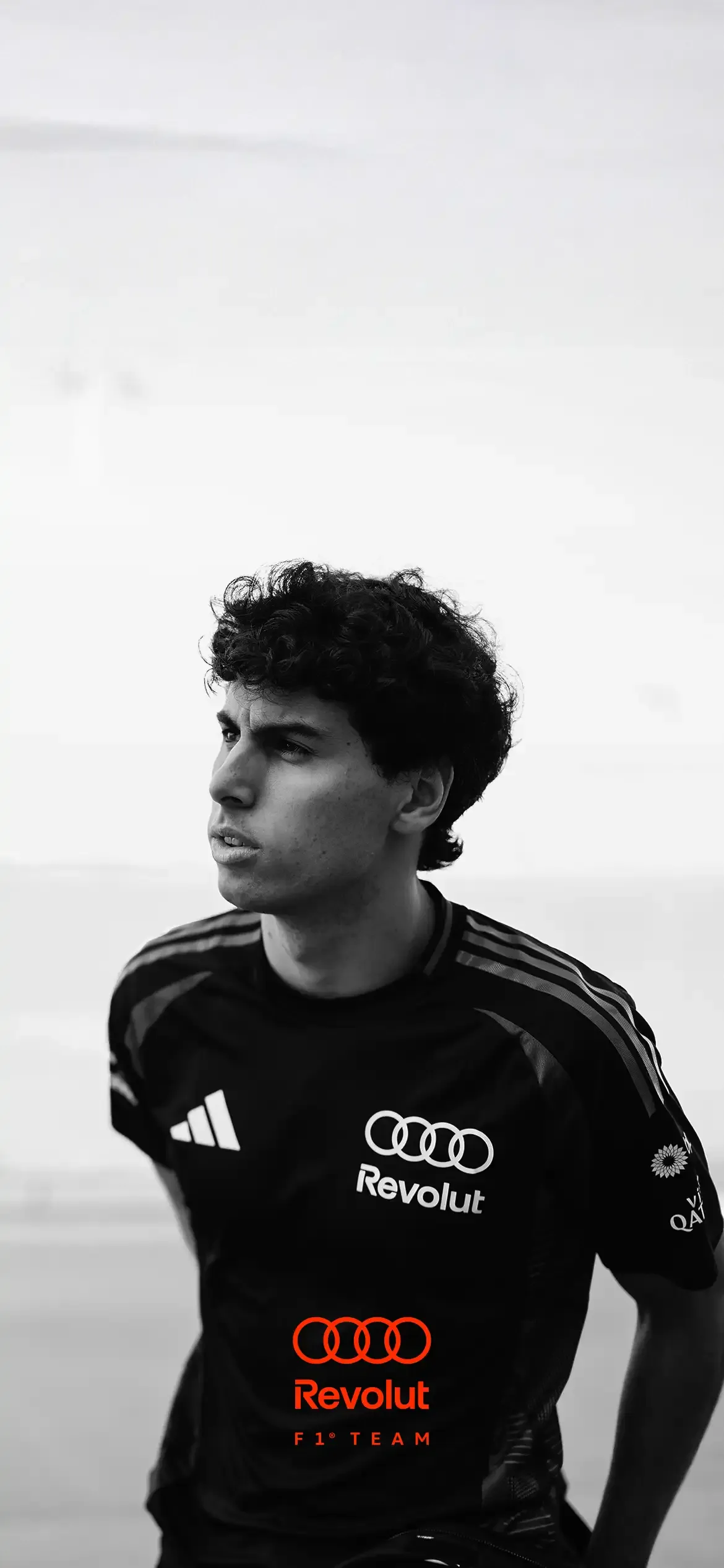 Black and white portrait foto of Audi Revolut F1® Team driver Gabriel Bortoleto wearing black crew tshirt with Adidas and Audi rings Logo