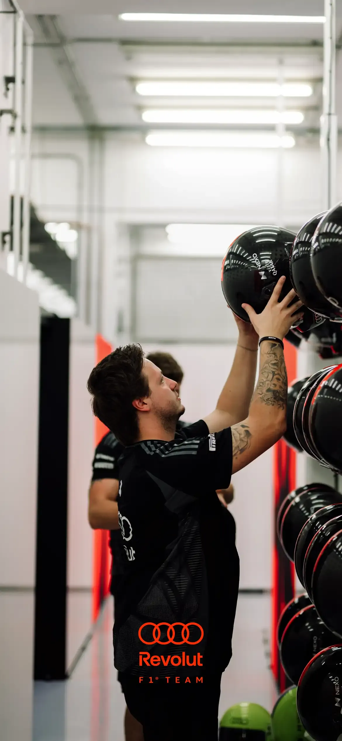 Inside the Audi Revolut F1® Team garage, showig crew members moving helmets from the wall
