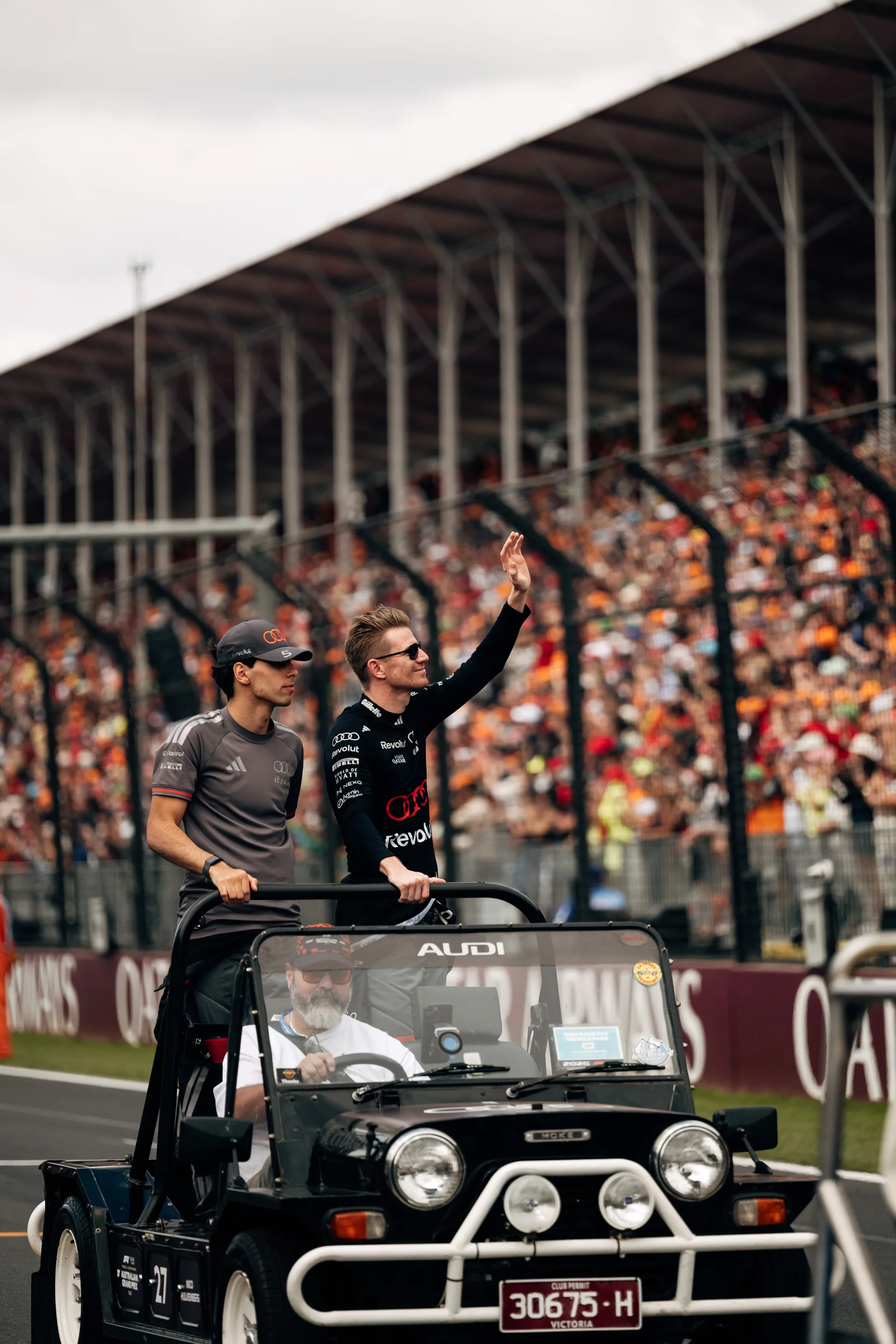 Close view of two Audi Revolut F1® Team drivers Nico Hulkenberg and Gabriel Bortoleto standing in a parade vehicle in front of the Melbourne grandstands.