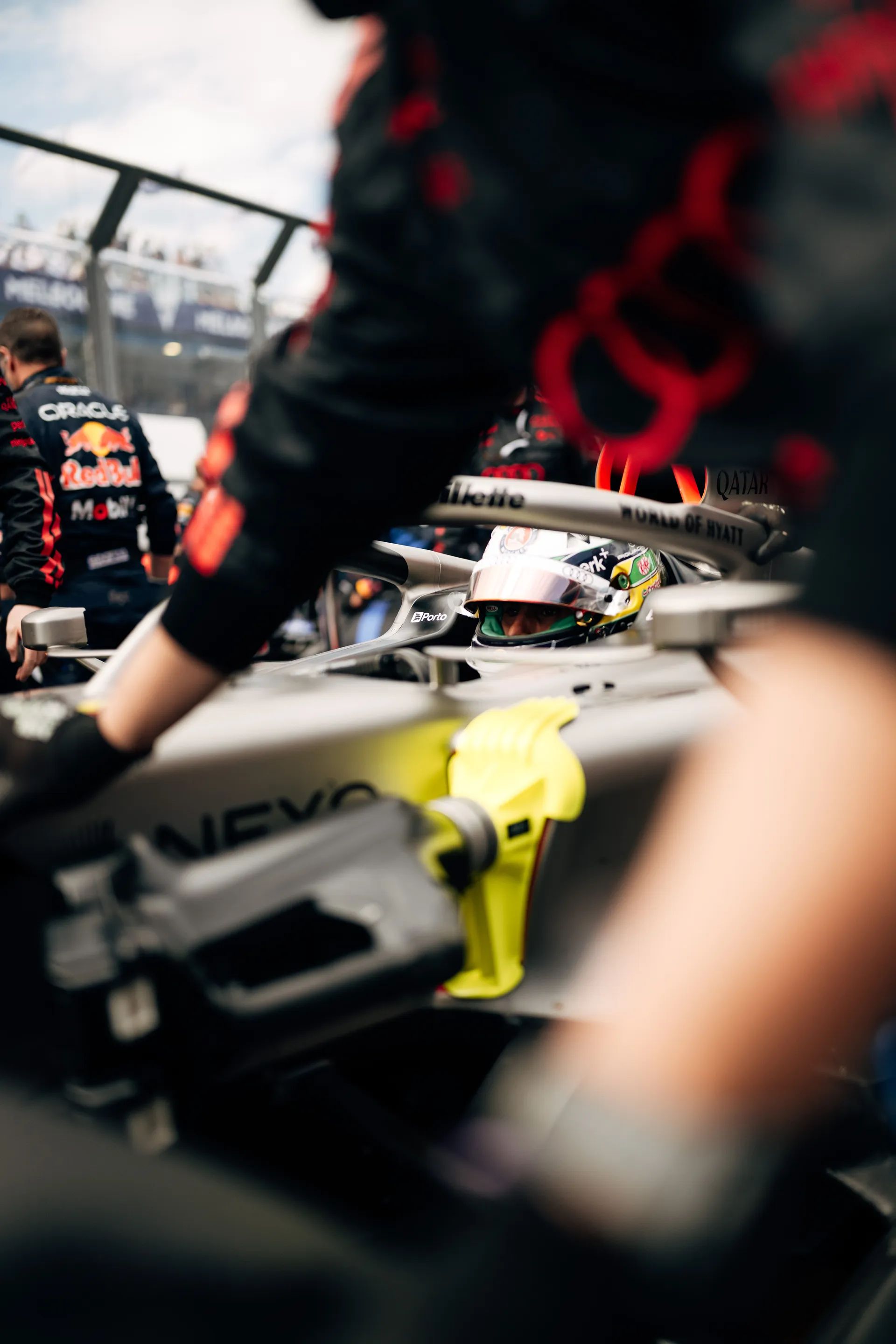 Helmeted Audi Revolut F1® Team driver Gabriel Bortoleto sits in the cockpit on the Melbourne grid, framed by mechanics and surrounding cars.