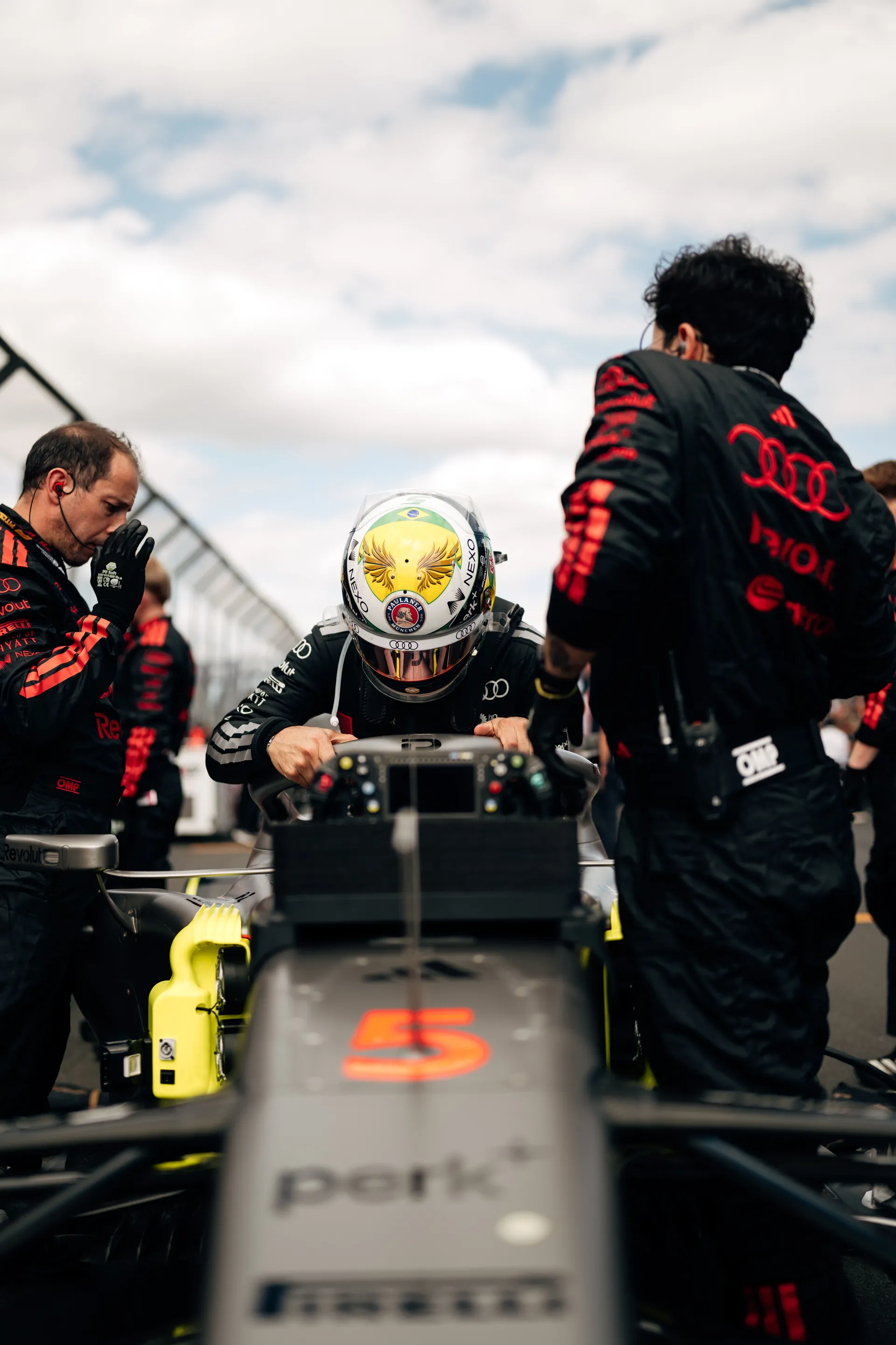 Audi Revolut F1® Team driver Gabriel Bortoleto sits in the cockpit of car number 5 while crew members make final preparations on the grid.