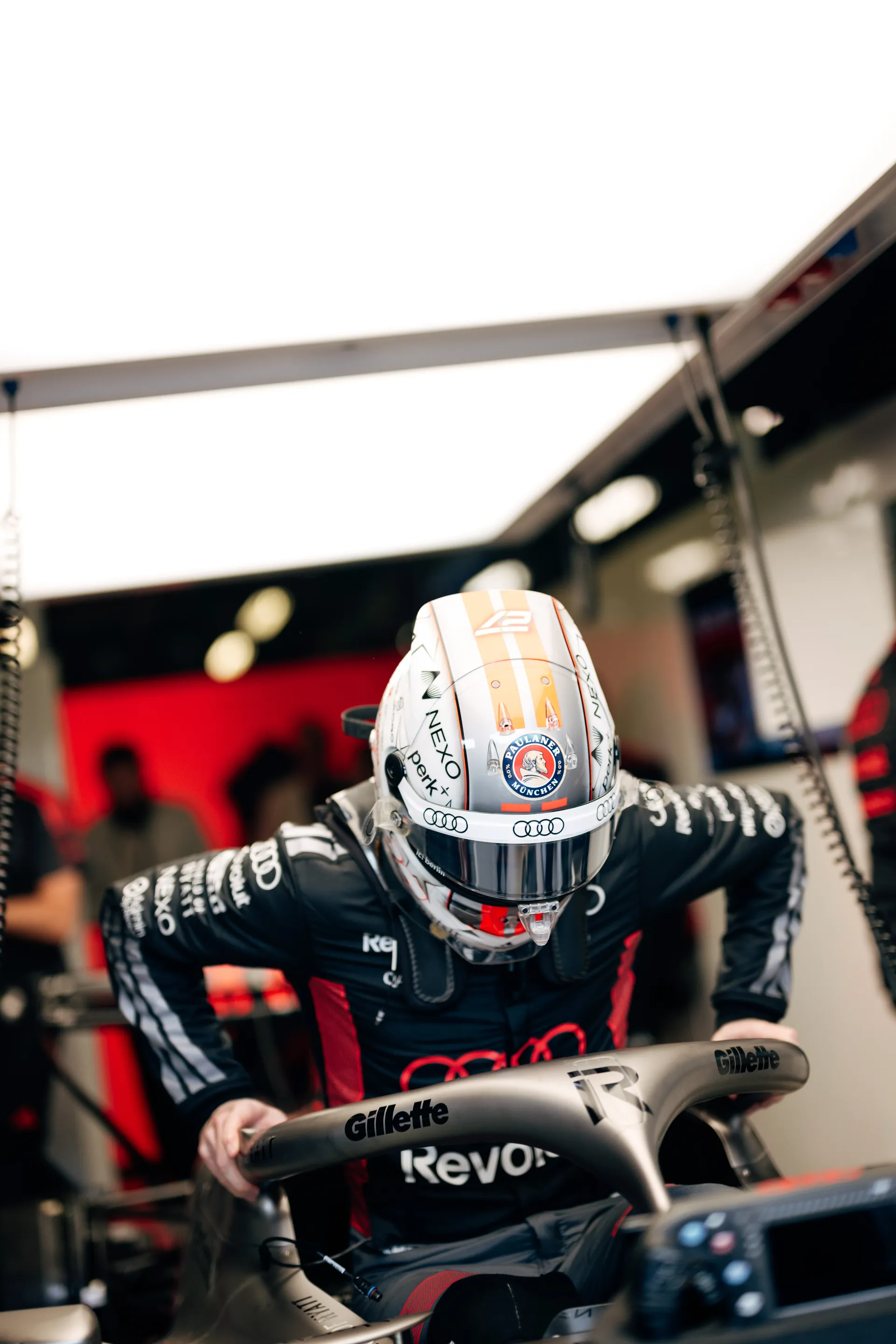 Helmeted Audi Revolut F1® Team driver Nico Hulkenberg leans into the cockpit inside the garage during qualifying setup.