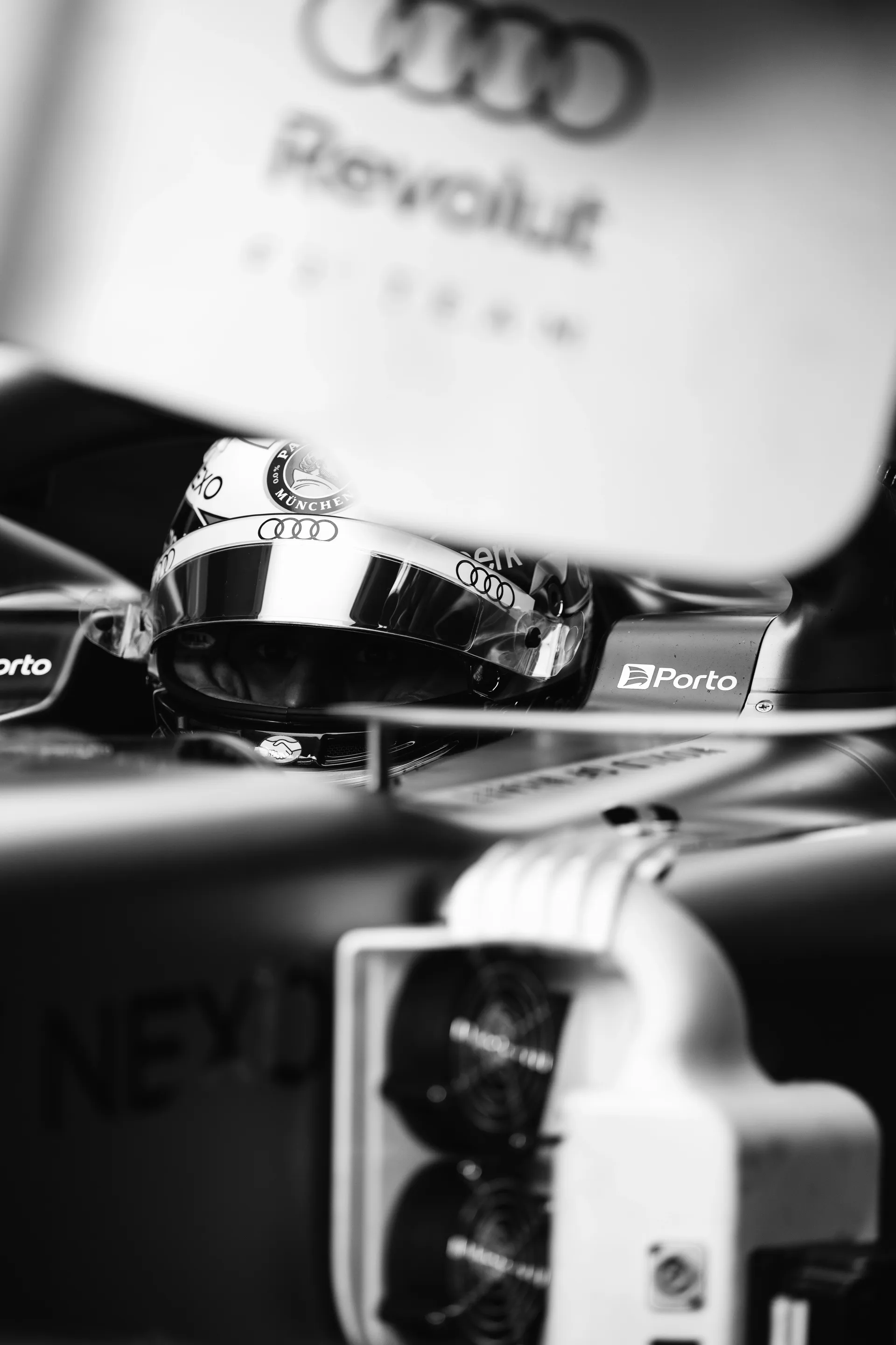 Black and white close up of an Audi Revolut F1® Team driver Nico Hulkenberg  helmet framed through garage equipment and car bodywork.