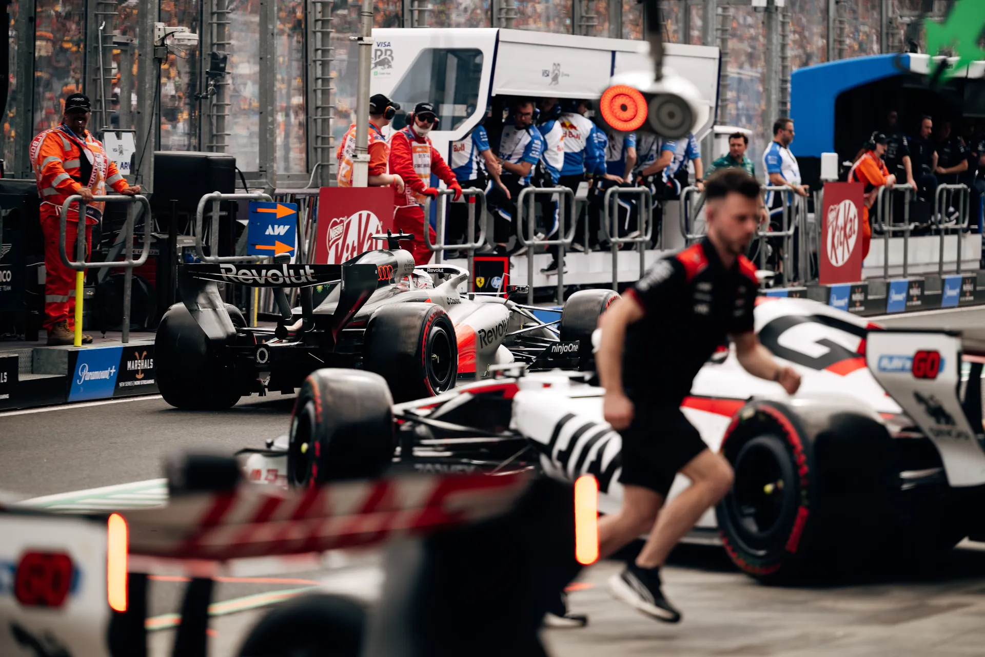 Audi Revolut F1® Team car waits in the pit lane among other Formula 1 cars and crew during a busy qualifying session.