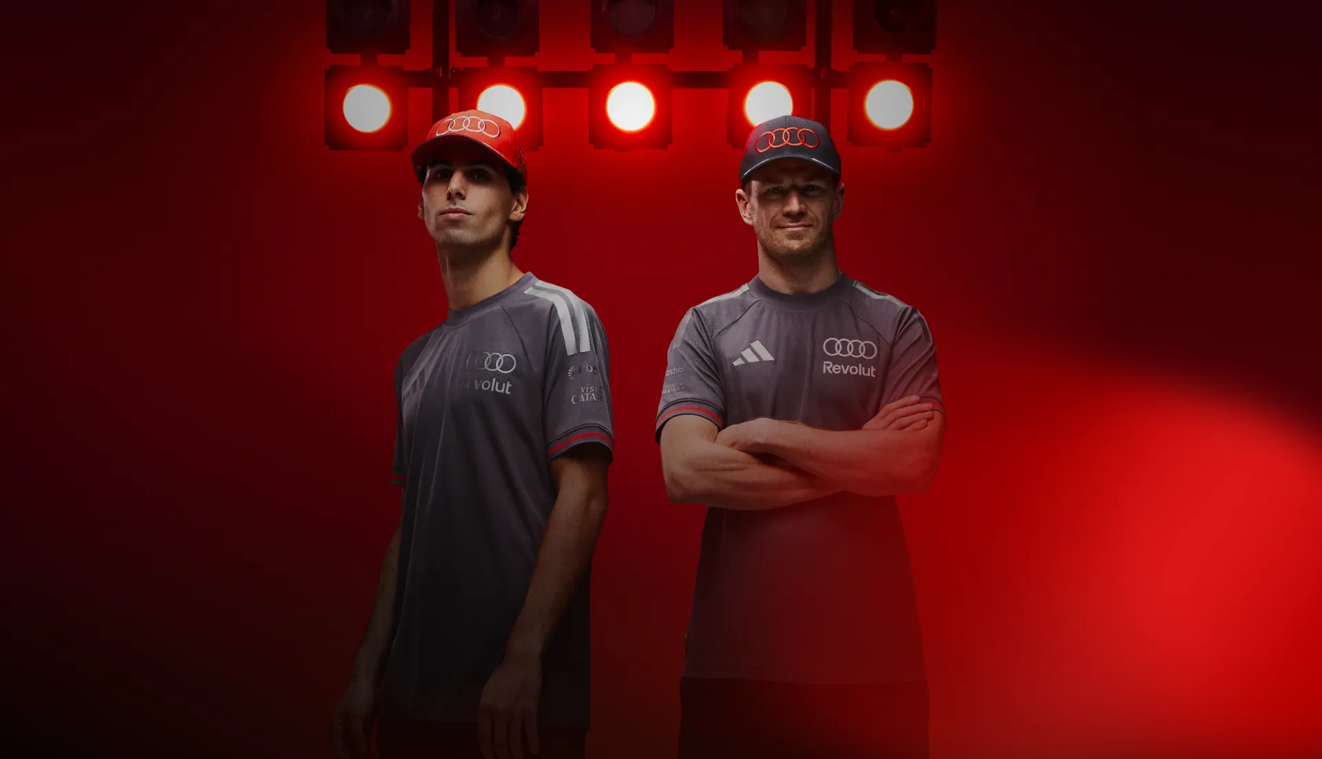 Two Formula 1 drivers Gabriel Bortoleto and Nico Hulkenberg standing half-portrait grey team shirts confident posture arms crossed second Nico Hulkenberg slightly offset professional motorsport team look red studio background