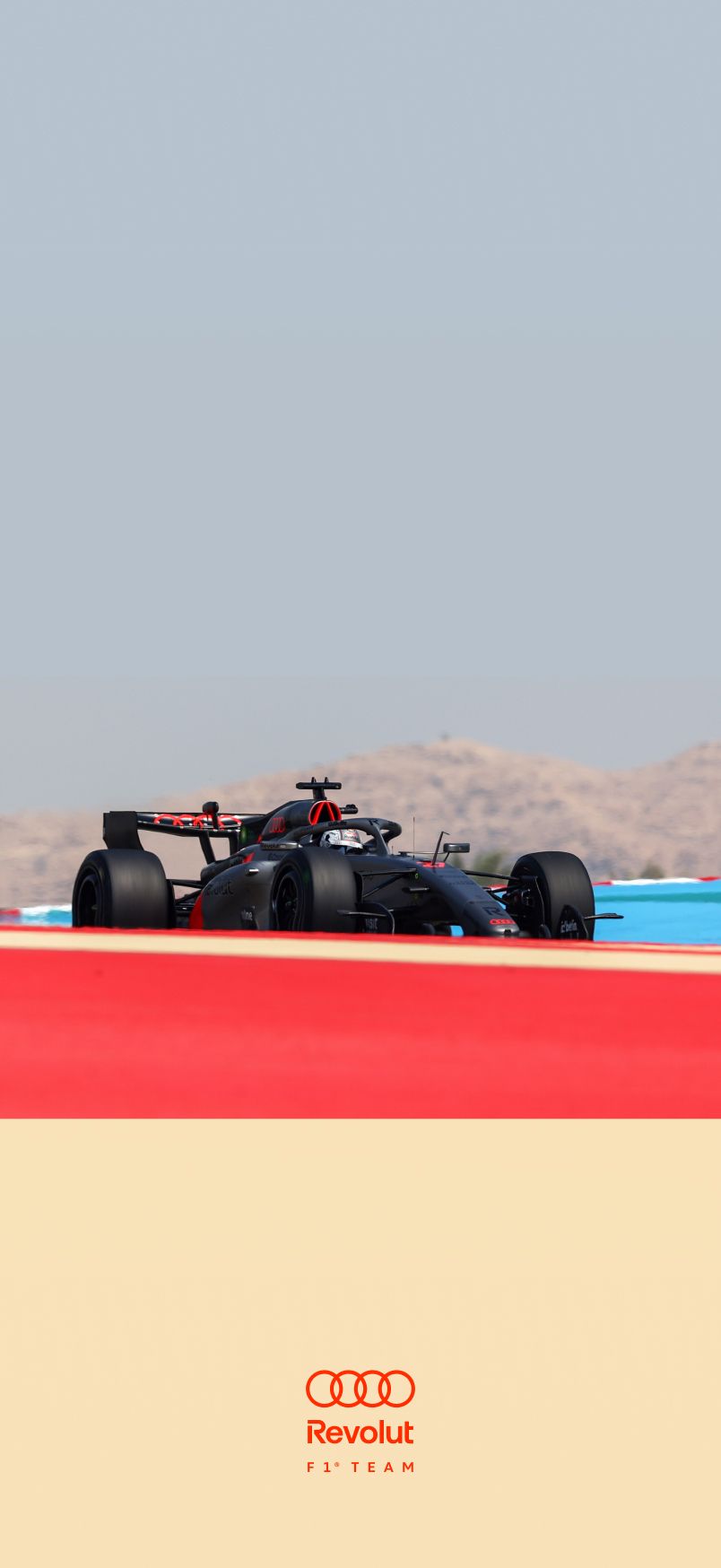 Audi Revolut F1® Team car race car on a racetrack in daylight, shot from a low angle; red painted track edge in the foreground, desert landscape and pale sky in the background.