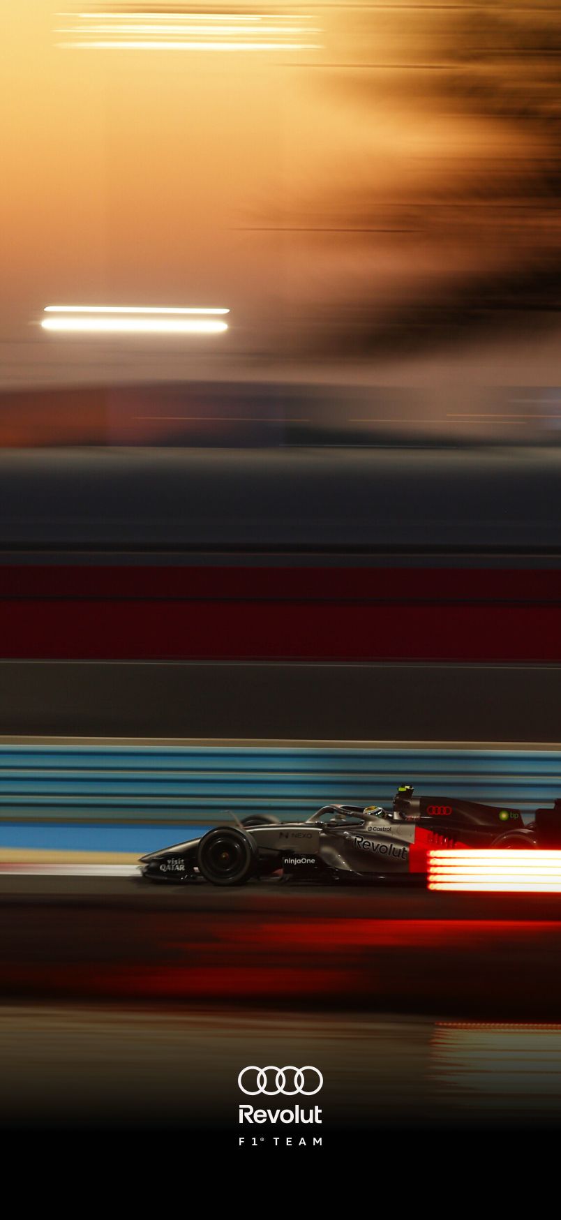 Sideview of the Audi Revolut F1® Team car speeding past with heavy horizontal motion blur; red, blue, and white light streaks emphasize high speed and nighttime racing atmosphere.