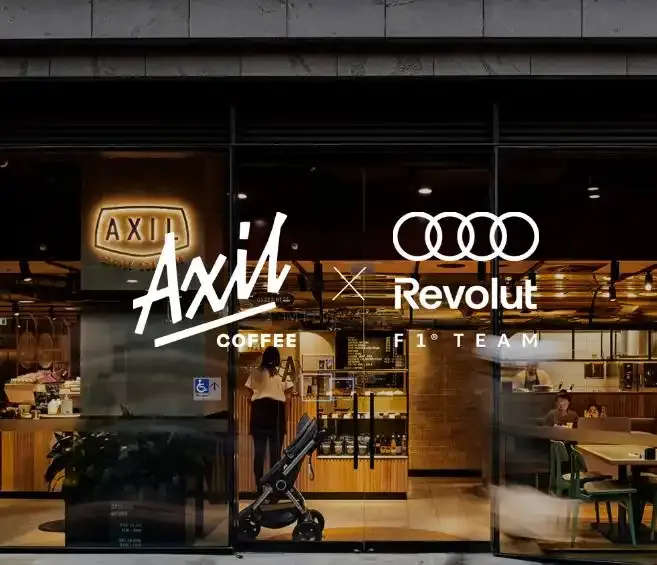 An image of a Axils coffe shop in the back with Adidas logo on the left and Audi Revolut F1® Team Logo on the right
