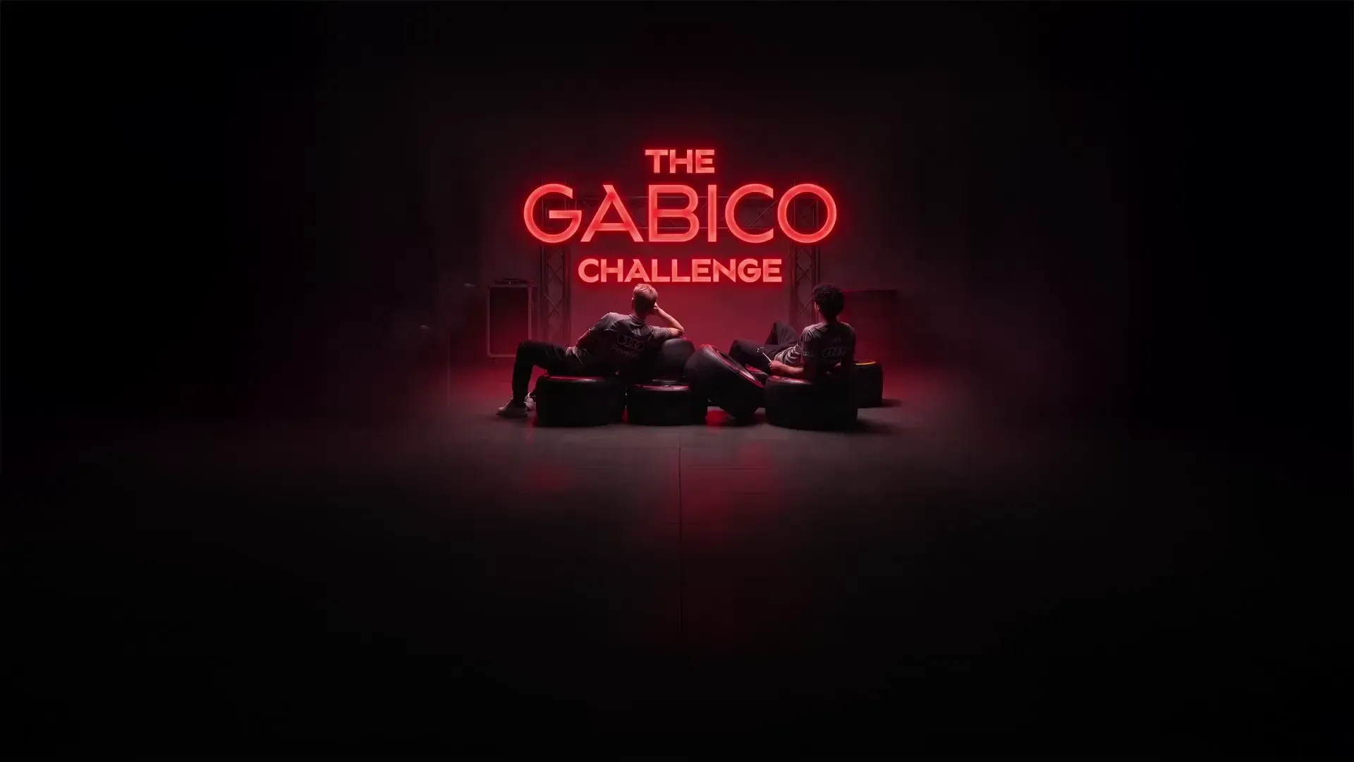 Audi Revolut F1® Team drivers Nico Hulkenberg and Gabriel Bortoleto sitting in a chill position in front of a GABICO neon sign in the garage