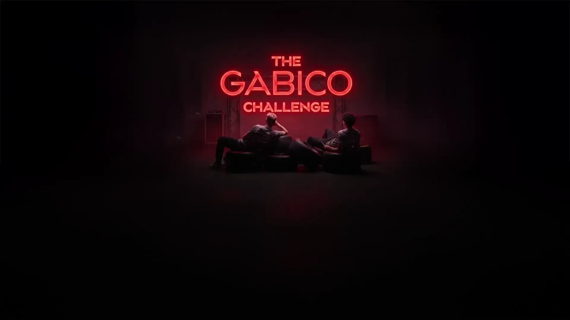 Audi Revolut F1® Team drivers Nico Hulkenberg and Gabriel Bortoleto sitting in a chill position in front of a GABICO neon sign in the garage