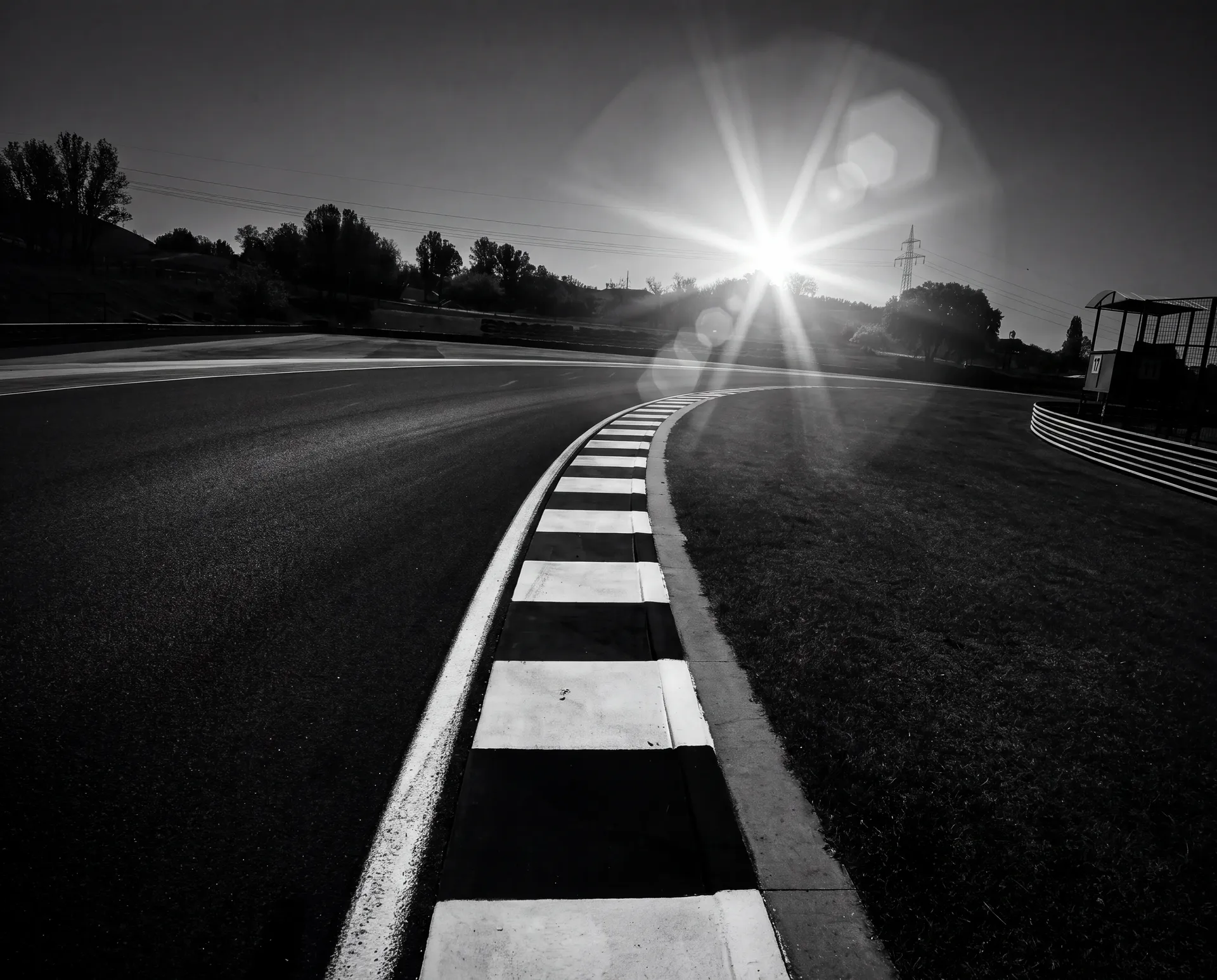 Low-angle black-and-white view of a Hungaroring kerb into Turn 17 with sun flare before the Audi Revolut F1® Team Hungarian GP