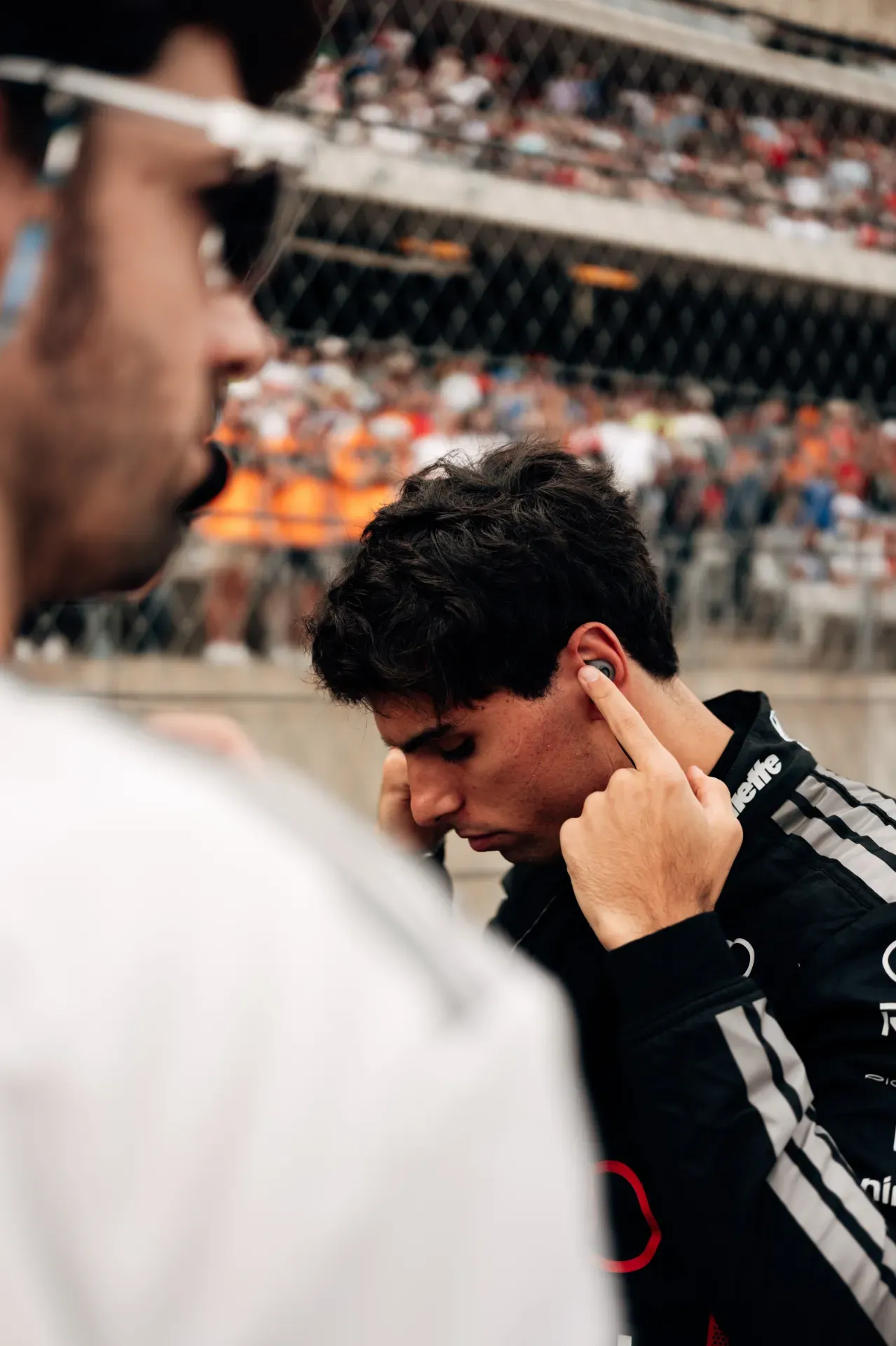 Gabriel Bortoleto of the Audi Revolut F1® Team adjusts an earpiece on the grid in Austin, a mechanic in white in front
