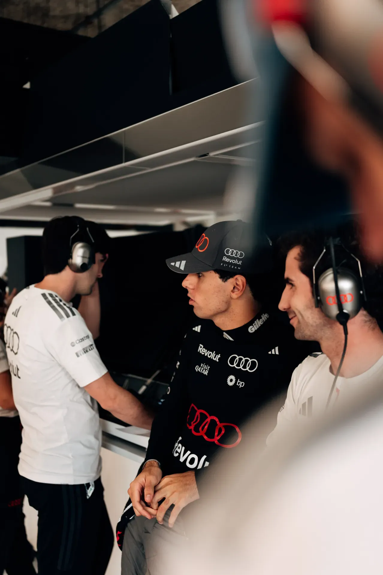 Gabriel Bortoleto and two mechanics of the Audi Revolut F1® Team wearing headsets in the garage in Austin