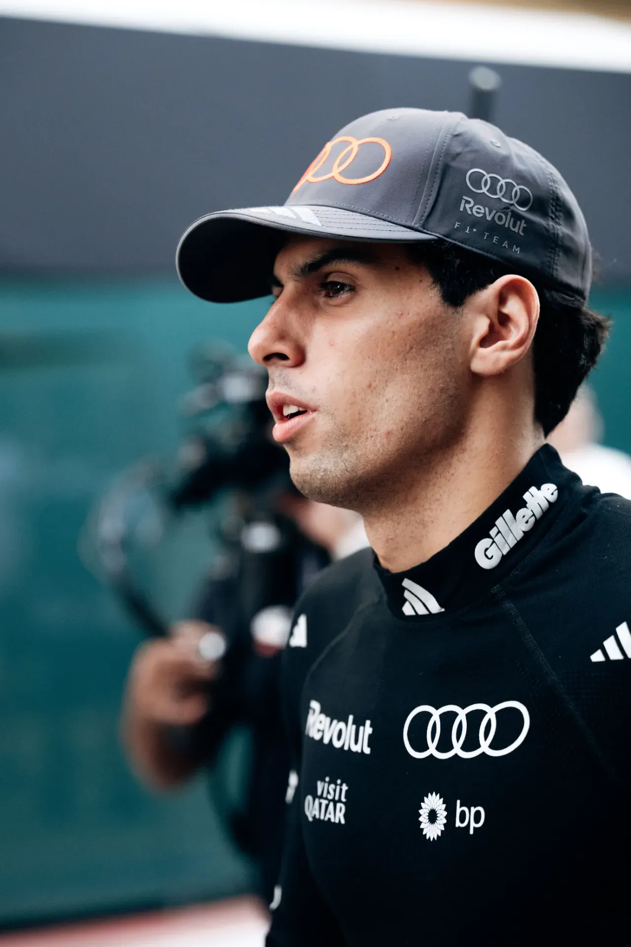 Gabriel Bortoleto of the Audi Revolut F1® Team in a grey team cap and black team top, in profile, with a camera operator behind in Austin