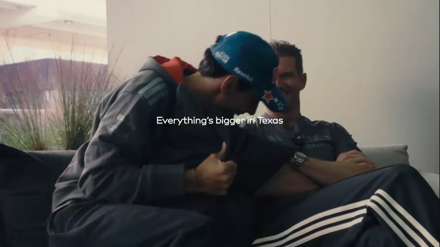 Gabriel Bortoleto in blue cap leans toward Nico Hulkenberg, arms crossed, on a sofa in Austin; text: Everything's bigger in Texas
