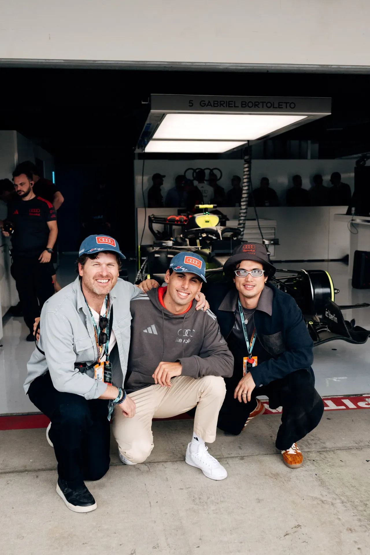 Gabriel Bortoleto and two fans crouch in front of a car in the garage of the Audi Revolut F1® Team in Austin