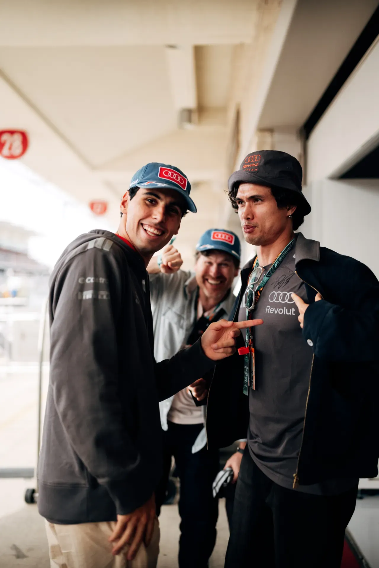 Gabriel Bortoleto in a blue Audi cap points at a fan in a bucket hat, with a fan in a blue cap behind, at the Audi Revolut F1® Team pit lane in Austin