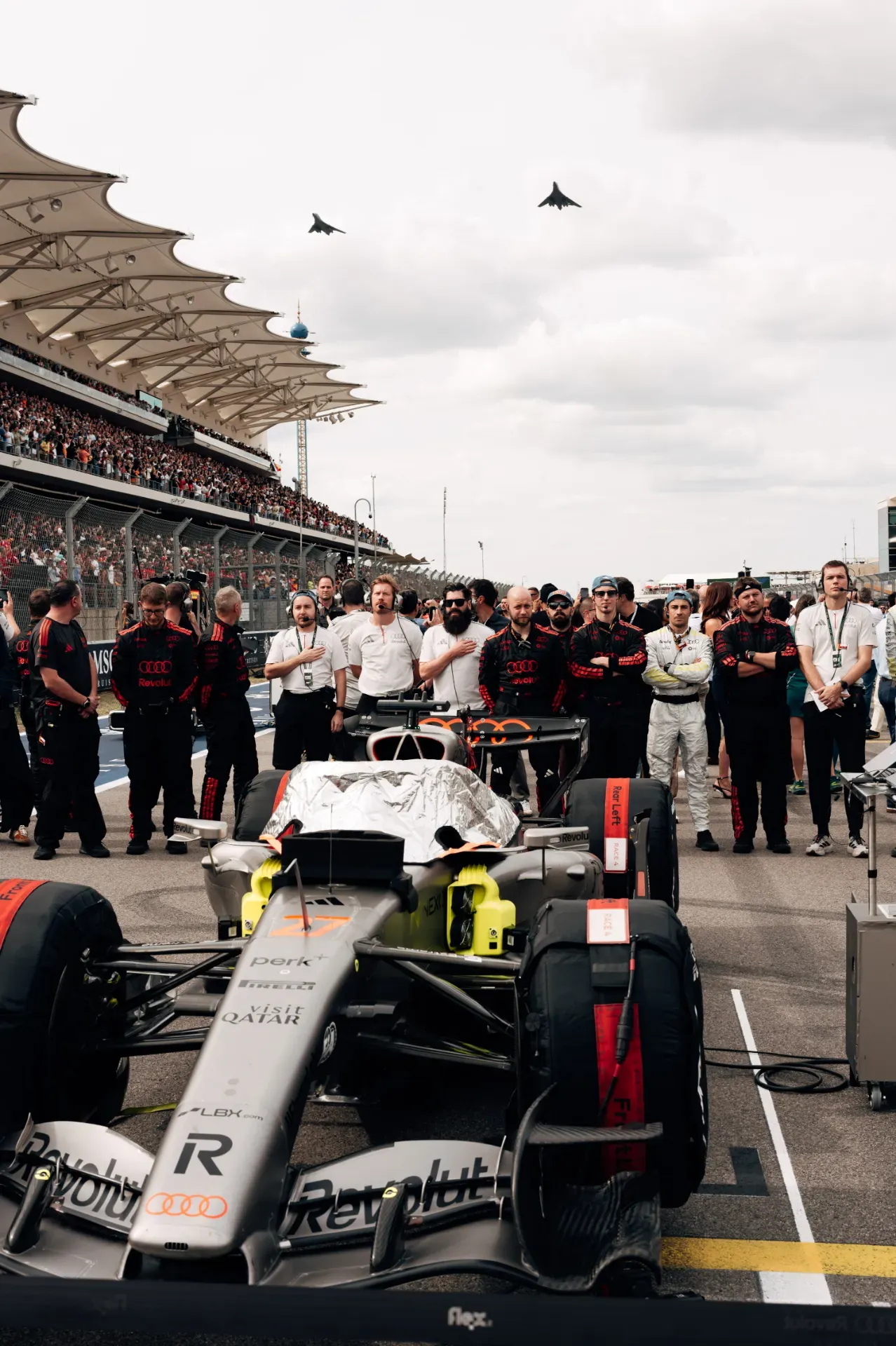 Car number 27 of the Audi Revolut F1® Team on the grid in Austin with team members standing behind and two jets flying overhead