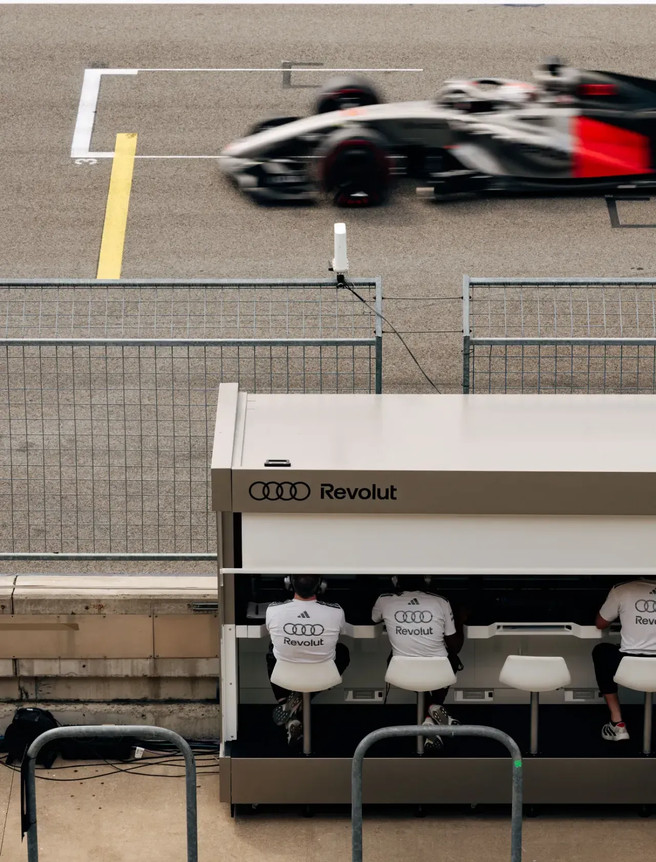 Car of the Audi Revolut F1® Team passes the pit wall with team members seated at the Audi Revolut pit stand in Austin